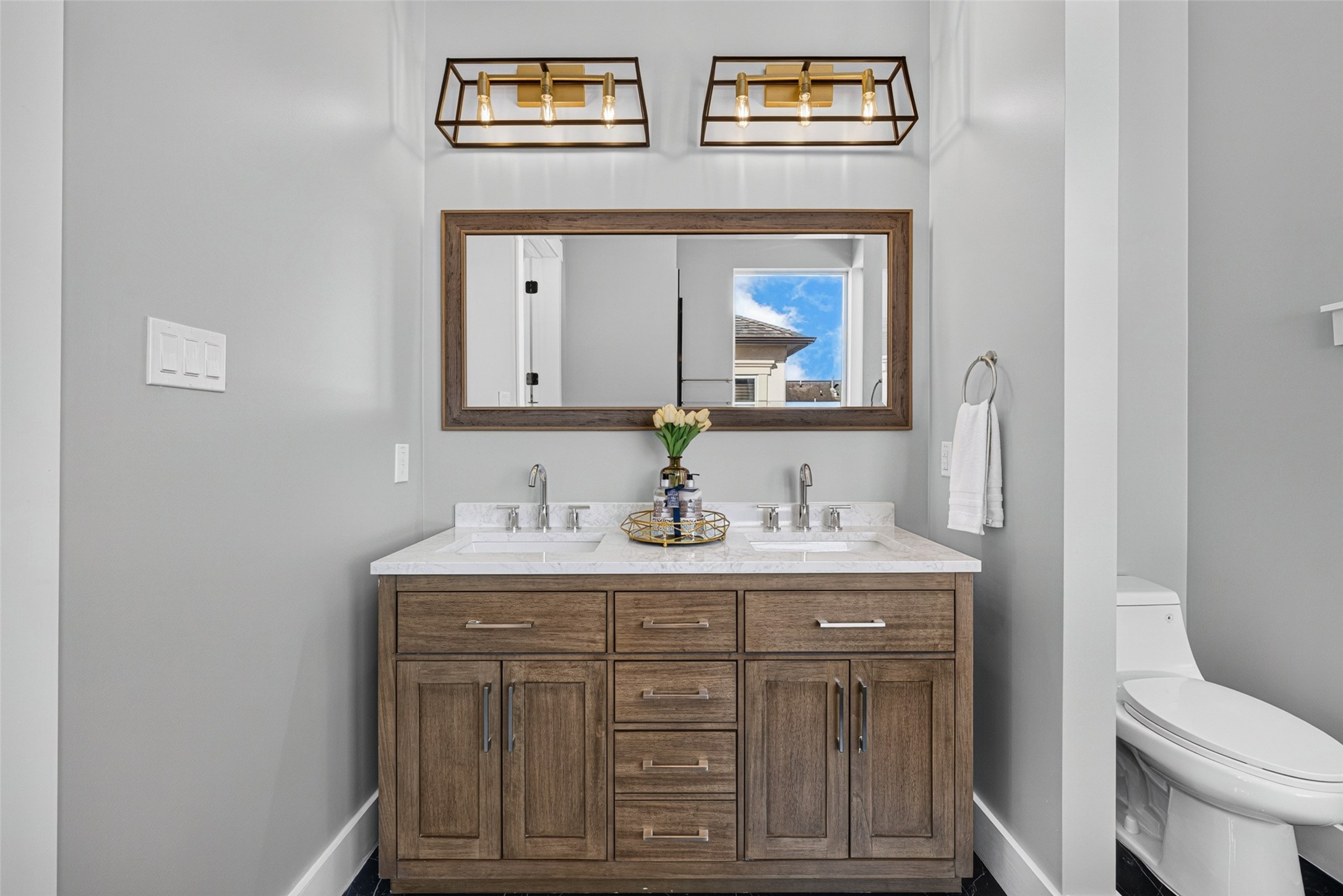 Spacious dual vanity featuring custom wood cabinetry, marble counters, dual sinks, and stylish overhead pendant lights.