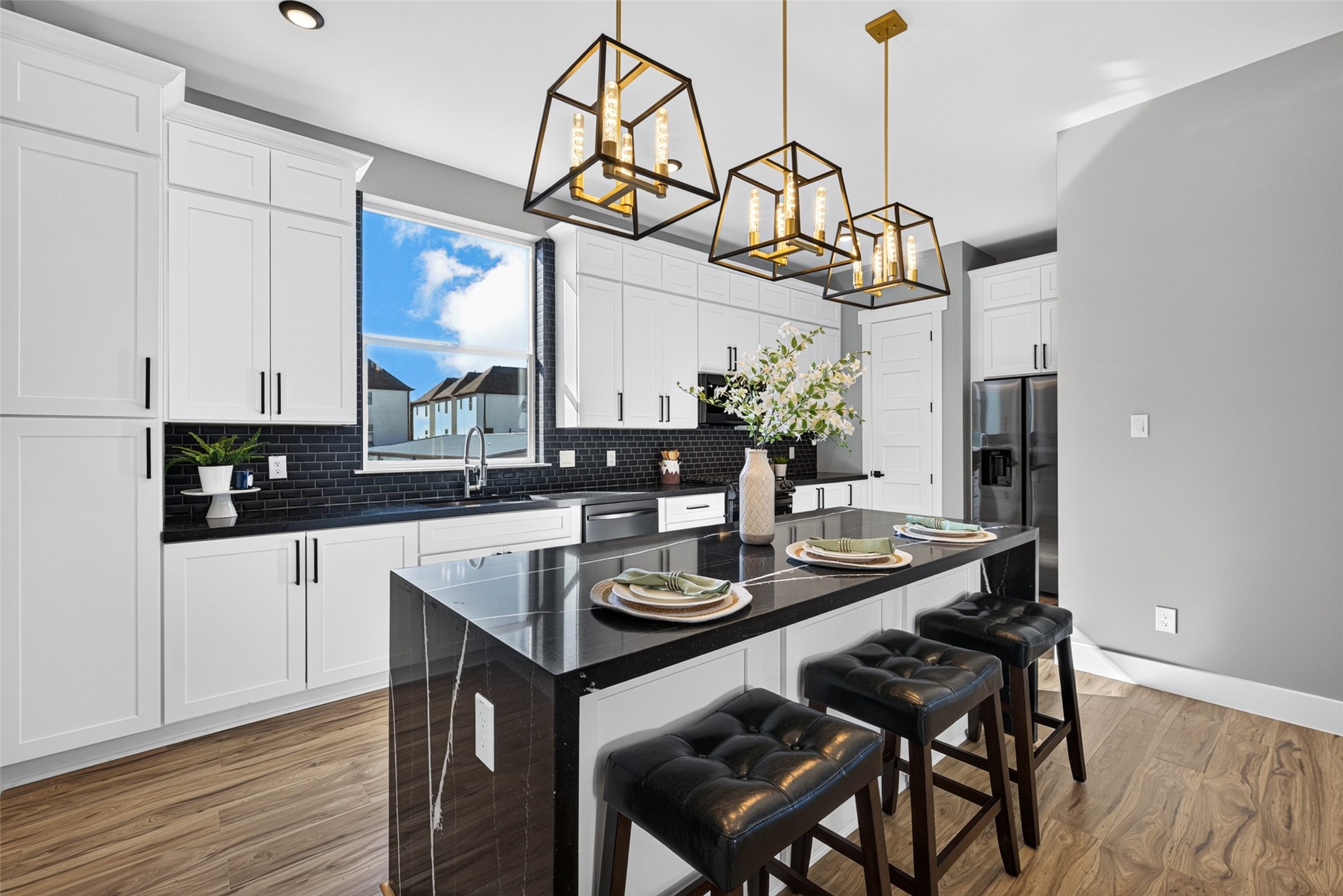 Beautiful dark tile backsplash and sleek white cabinetry contrast elegantly with the rich granite countertops and warm wood flooring
