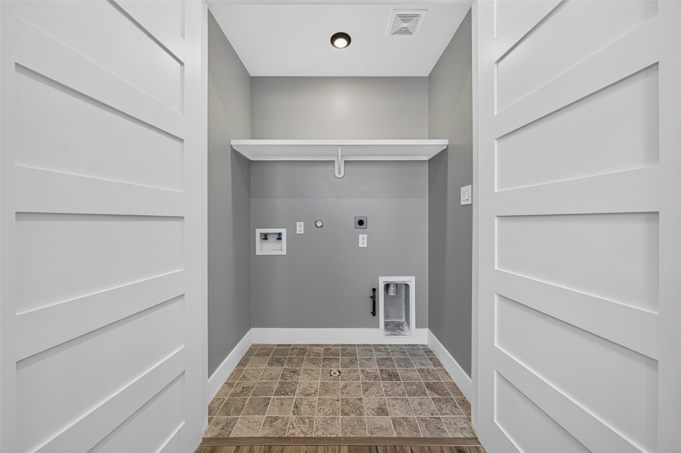 Convenient laundry area equipped with washer/dryer hookups, built-in storage shelf, and durable tile flooring.