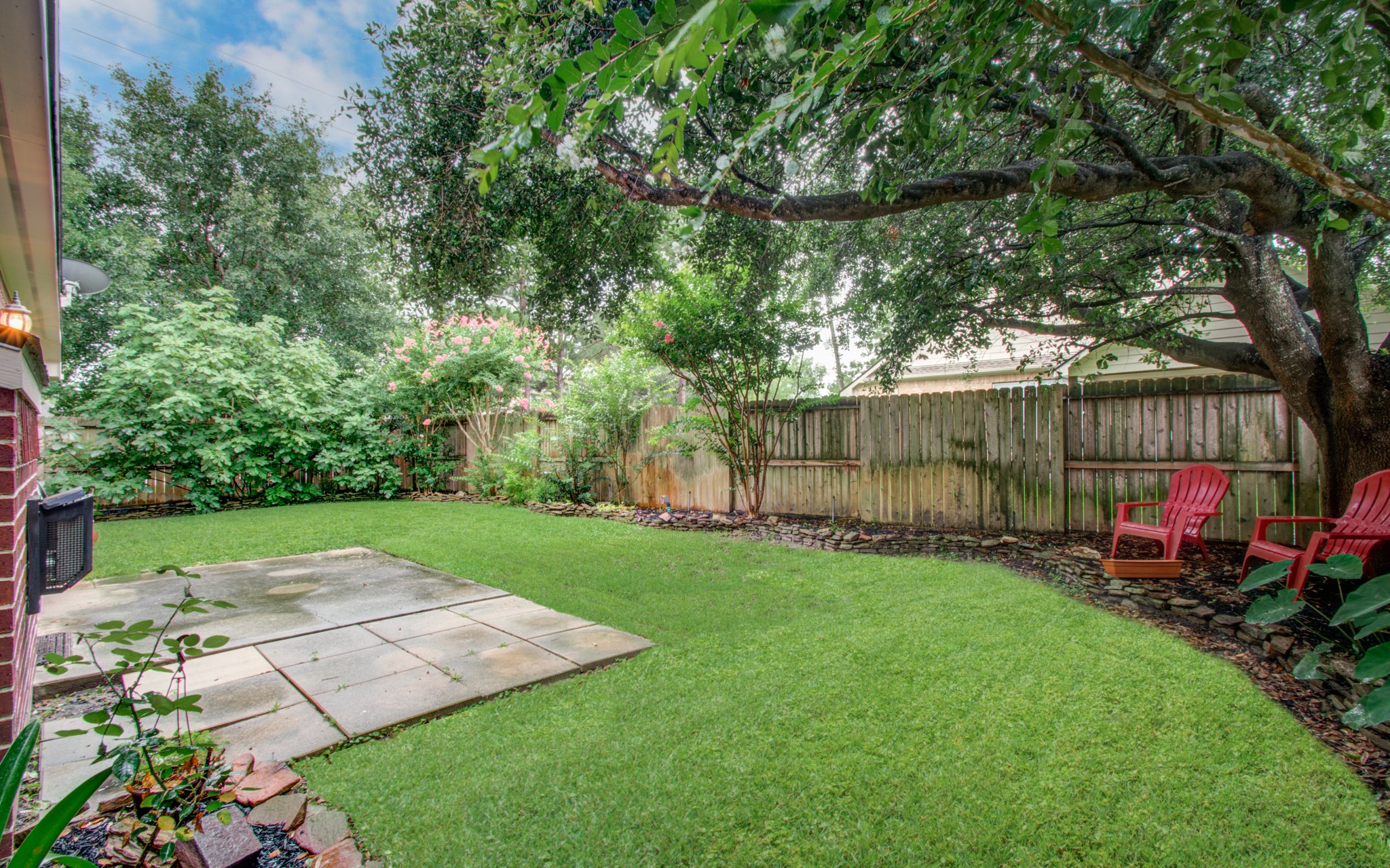 Tranquil backyard oasis with lush greenery, a spacious patio, and cozy seating under the shade of mature trees.
