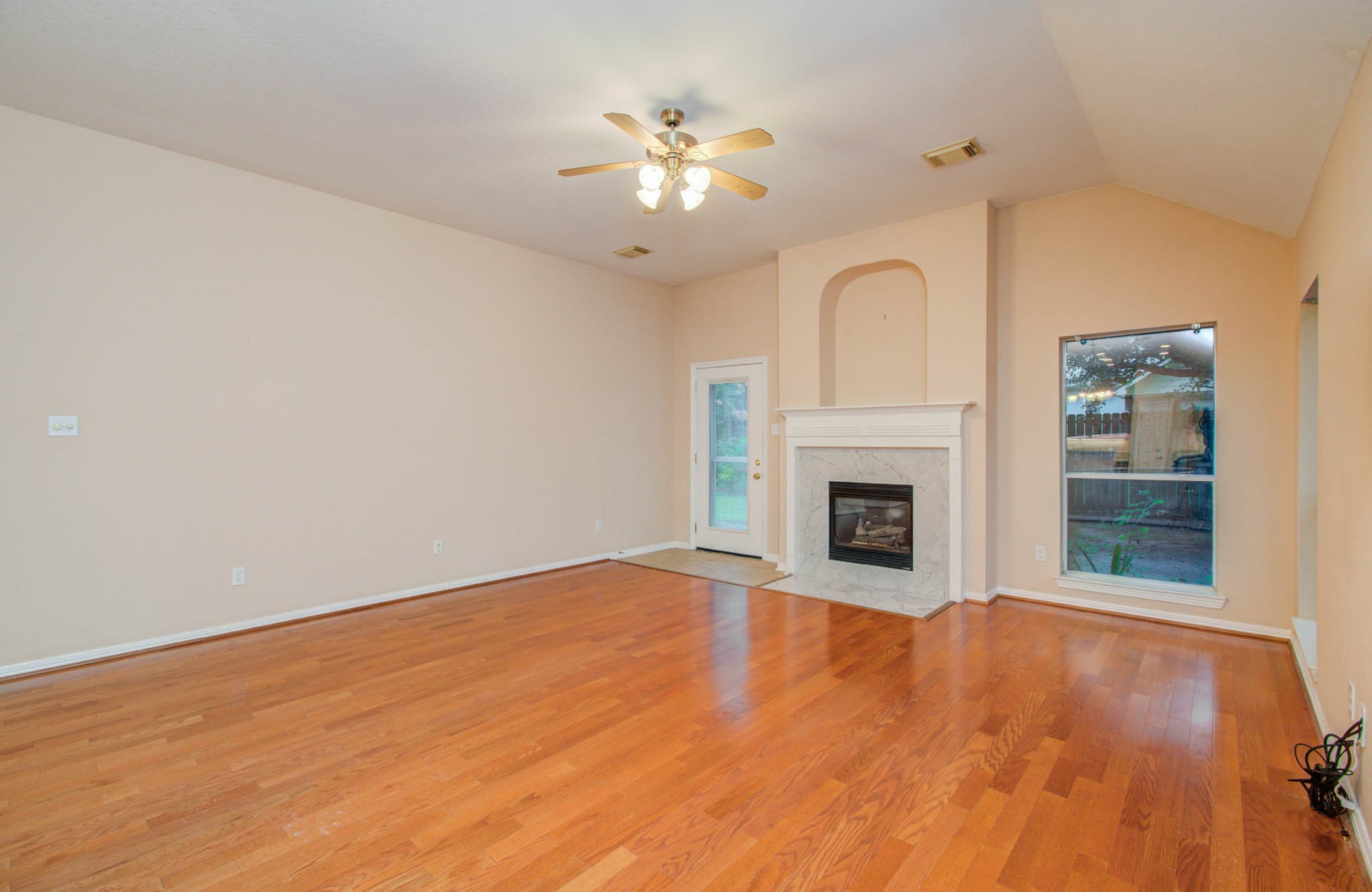 Spacious living room featuring elegant hardwood floors, a cozy fireplace with a classic mantle, and abundant natural light pouring in through large windows and a glass door.