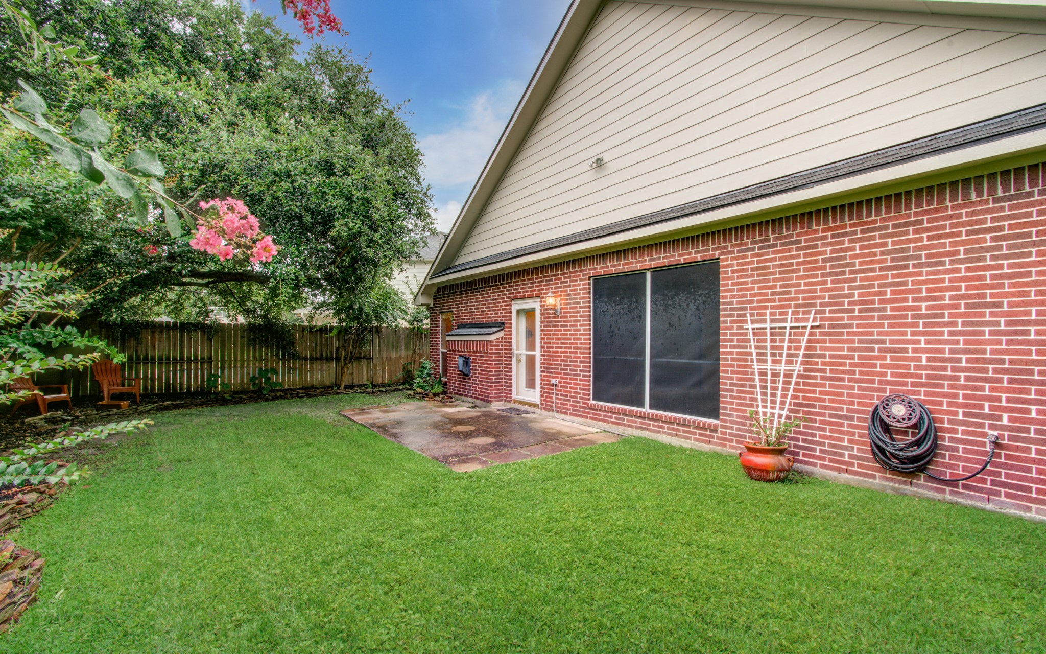 Charming backyard with lush green lawn, mature trees, and a cozy patio area perfect for relaxation or entertaining.