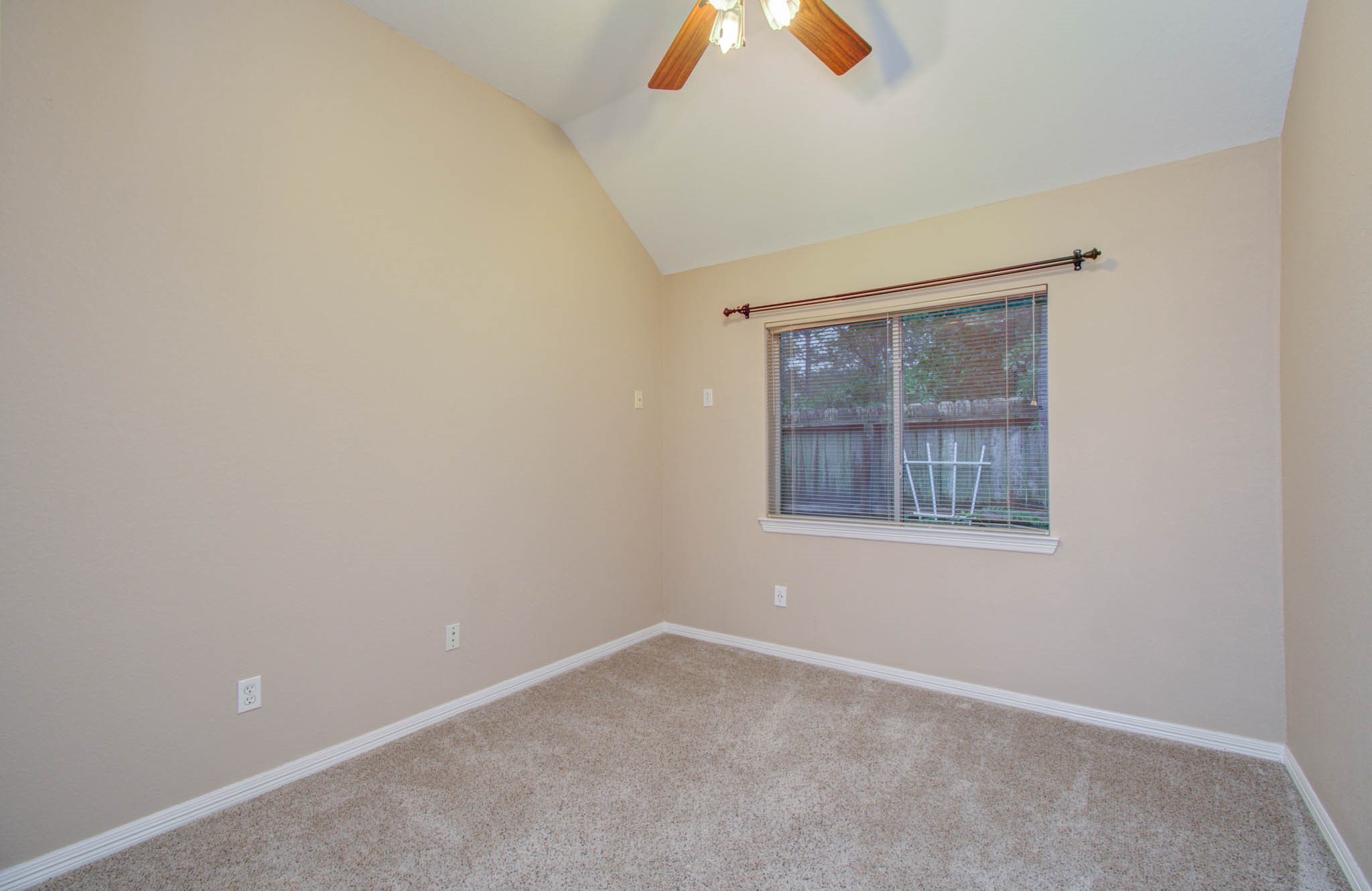 Cozy bedroom with soft carpeting, neutral walls, and a ceiling fan, offering a peaceful view through a large window.