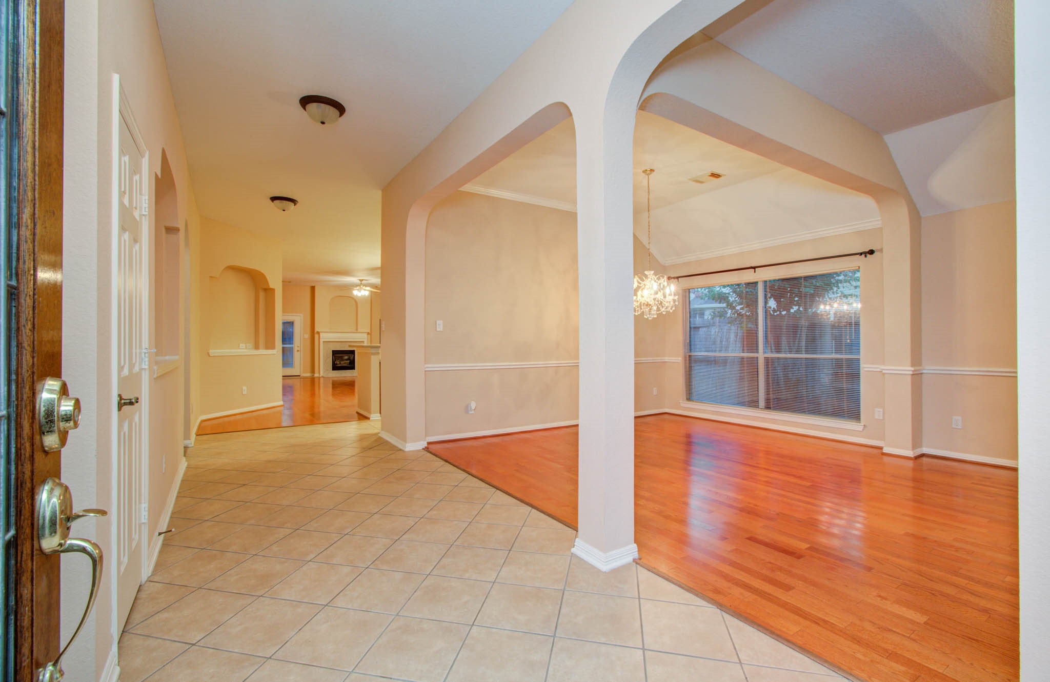 Elegant entryway with tile flooring and archways, seamlessly leading to a bright dining area featuring hardwood floors and a stunning chandelier.