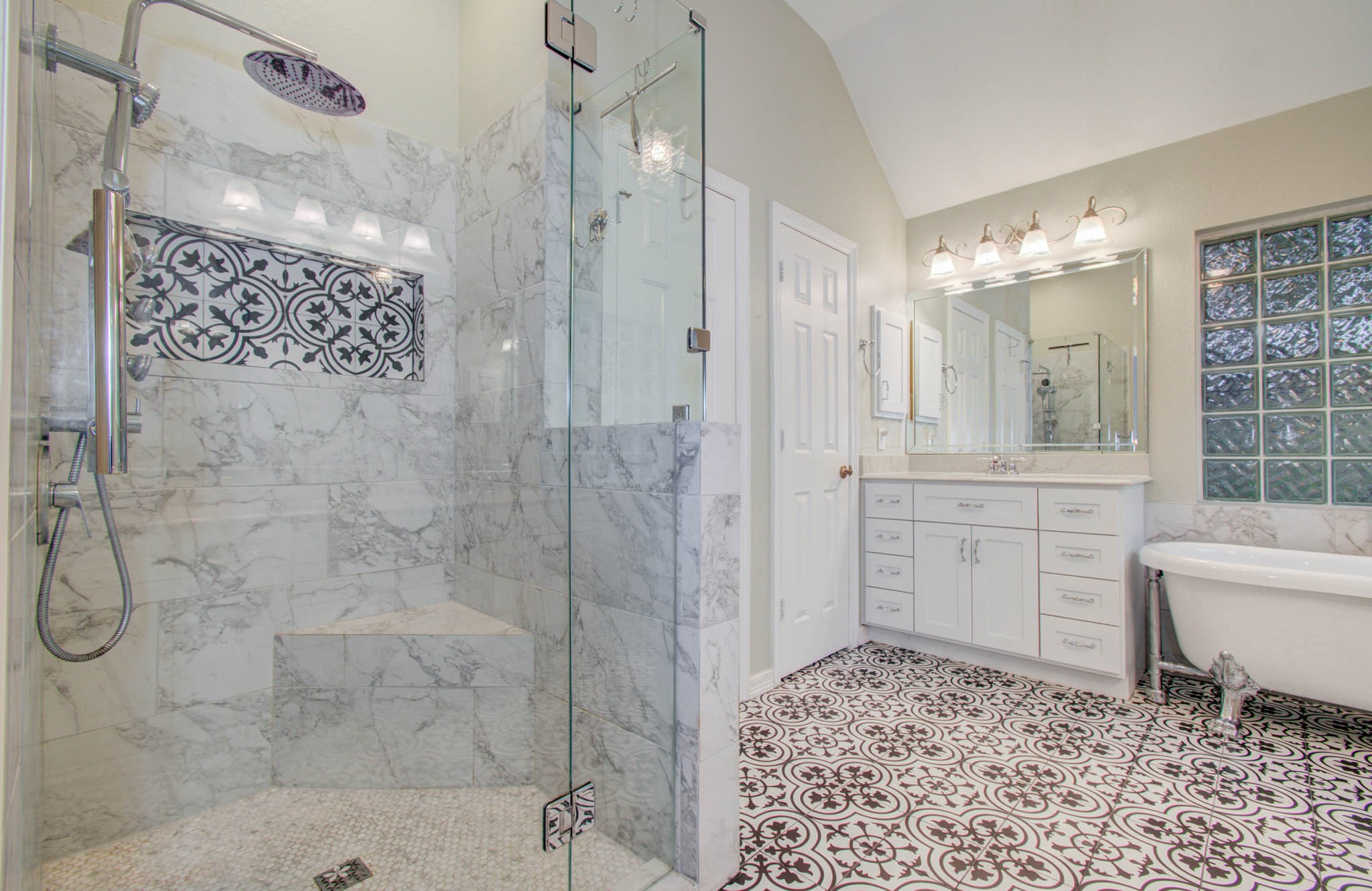 Elegant bathroom featuring a spacious glass-enclosed marble shower, intricate tile flooring, and a classic clawfoot tub, complemented by a stylish vanity with ample storage.