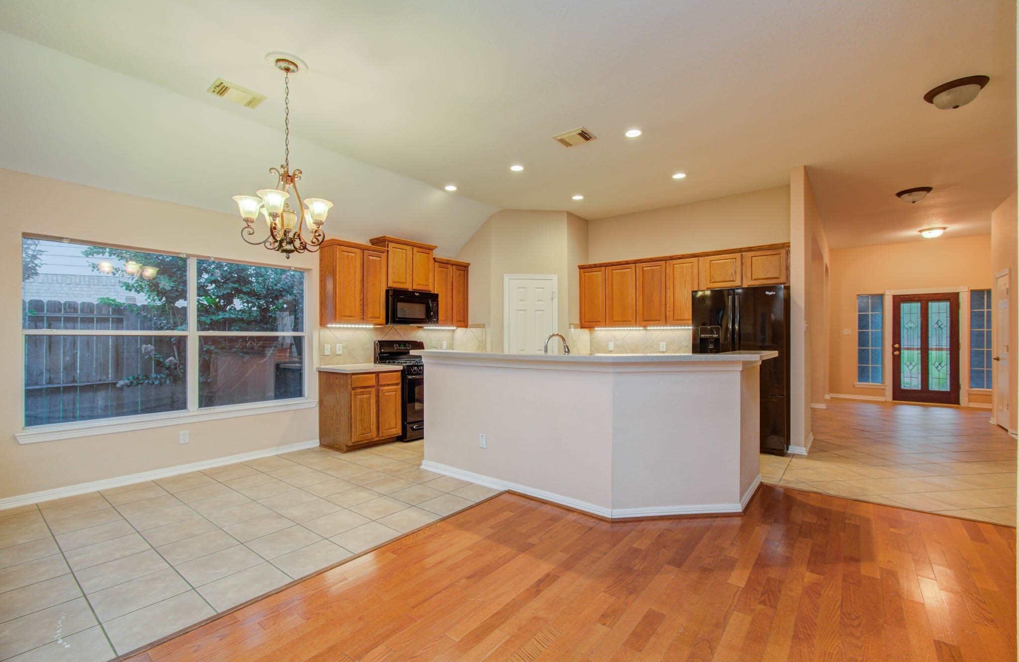 Spacious open-concept kitchen with warm wood cabinetry, modern appliances, and a large island, seamlessly flowing into a bright dining area with a charming chandelier.
