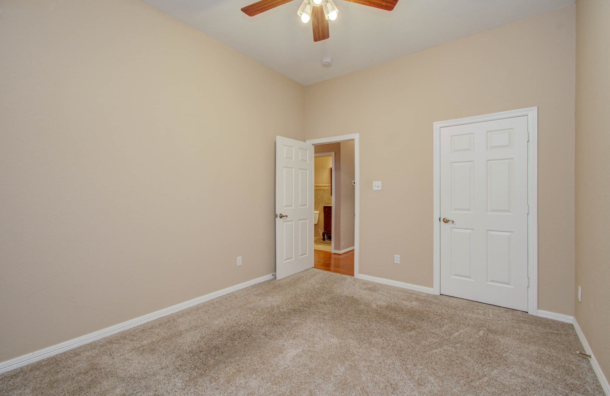 Cozy room with neutral walls, plush carpet, and ceiling fan, offering ample space and two doors for convenient access.