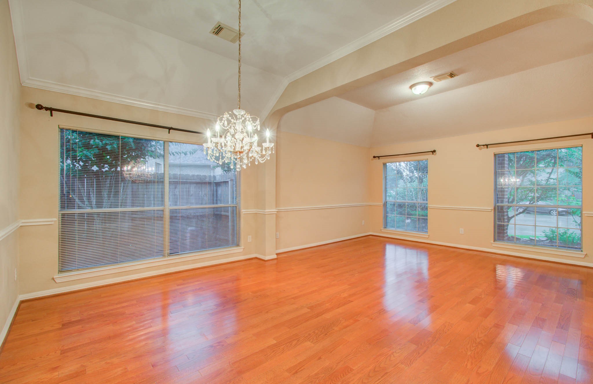 Elegant dining area with rich hardwood floors, abundant natural light from large windows, and a stunning chandelier, perfect for entertaining.