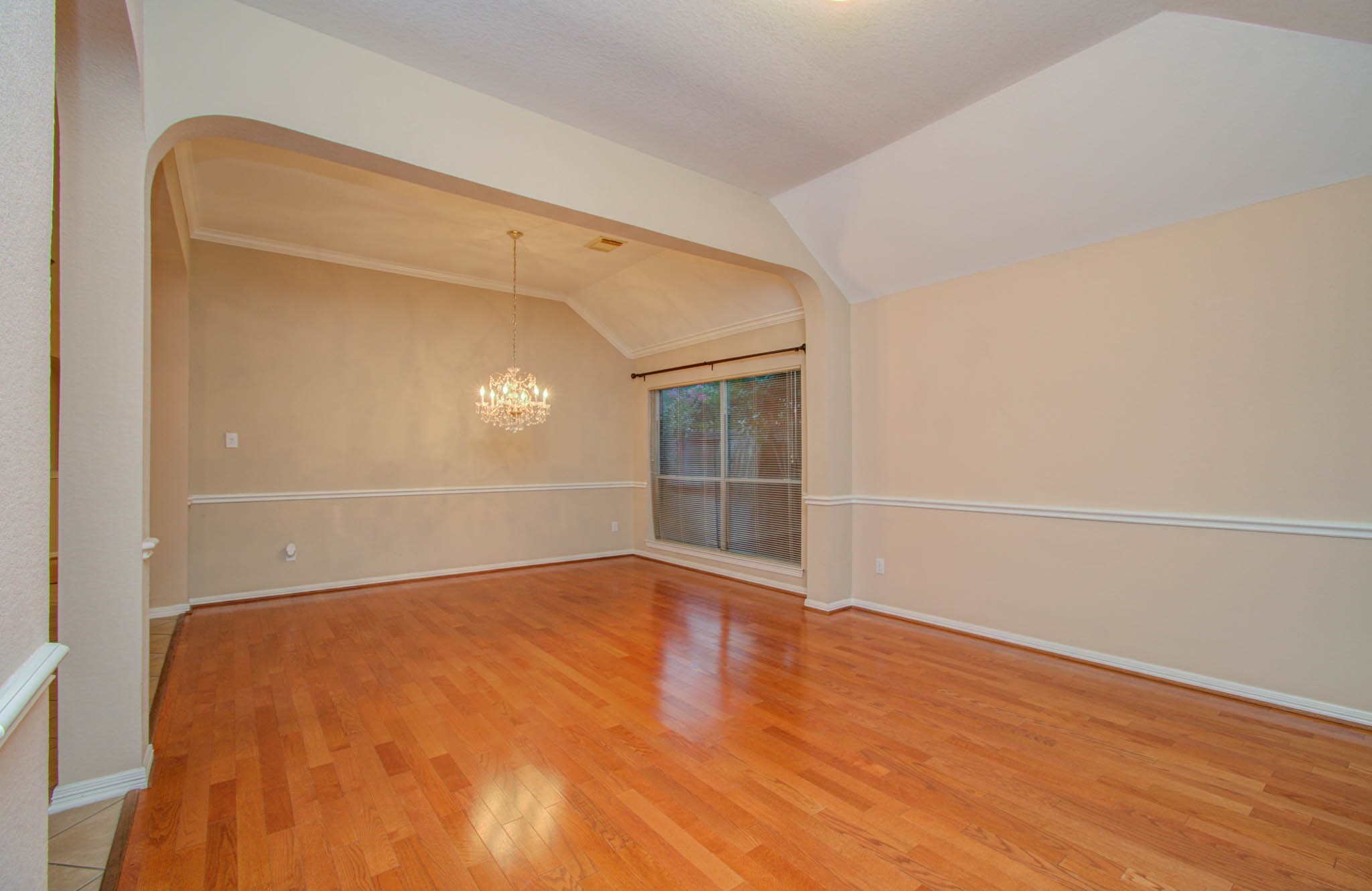 Spacious dining area with elegant hardwood floors, a stylish chandelier, and large windows providing ample natural light.