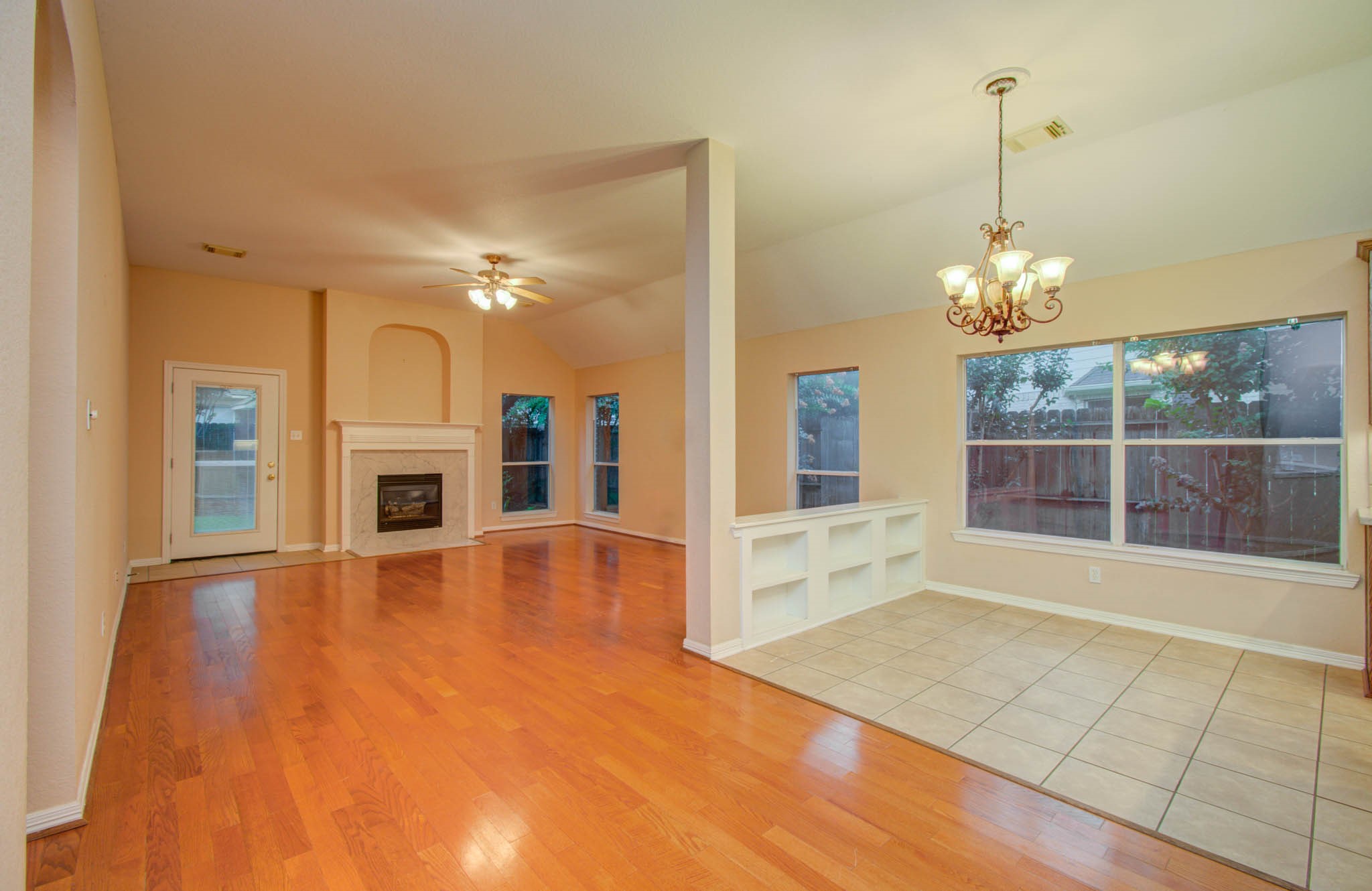 Spacious open-concept living area featuring gleaming hardwood floors, a cozy fireplace, and abundant natural light from large windows.