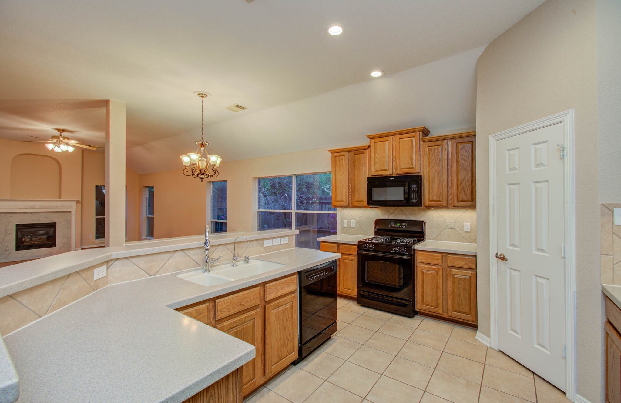 Spacious kitchen with warm wood cabinetry, sleek black appliances, and a convenient breakfast bar, seamlessly connecting to a cozy living area with a fireplace.