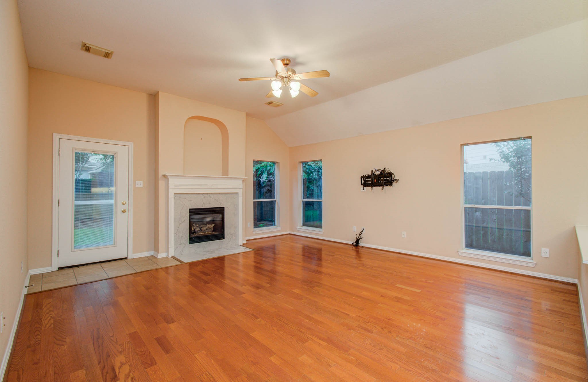 Spacious living room with warm hardwood floors, a cozy fireplace, and abundant natural light from large windows, offering a welcoming atmosphere.