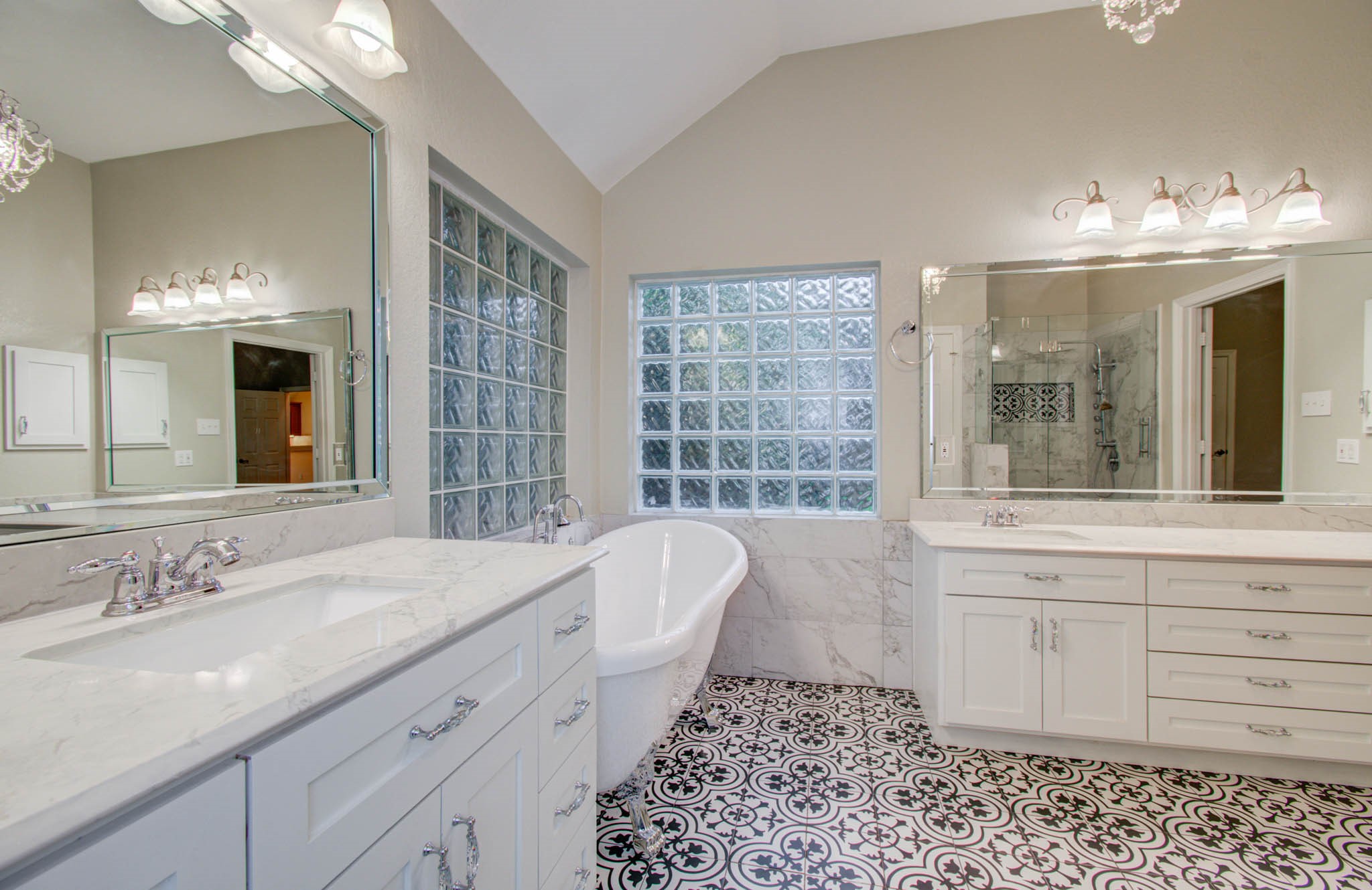 Stunning bathroom featuring a luxurious freestanding tub, elegant dual vanities with marble countertops, and a spacious glass-enclosed shower, all highlighted by stylish patterned tile flooring and ample natural light.