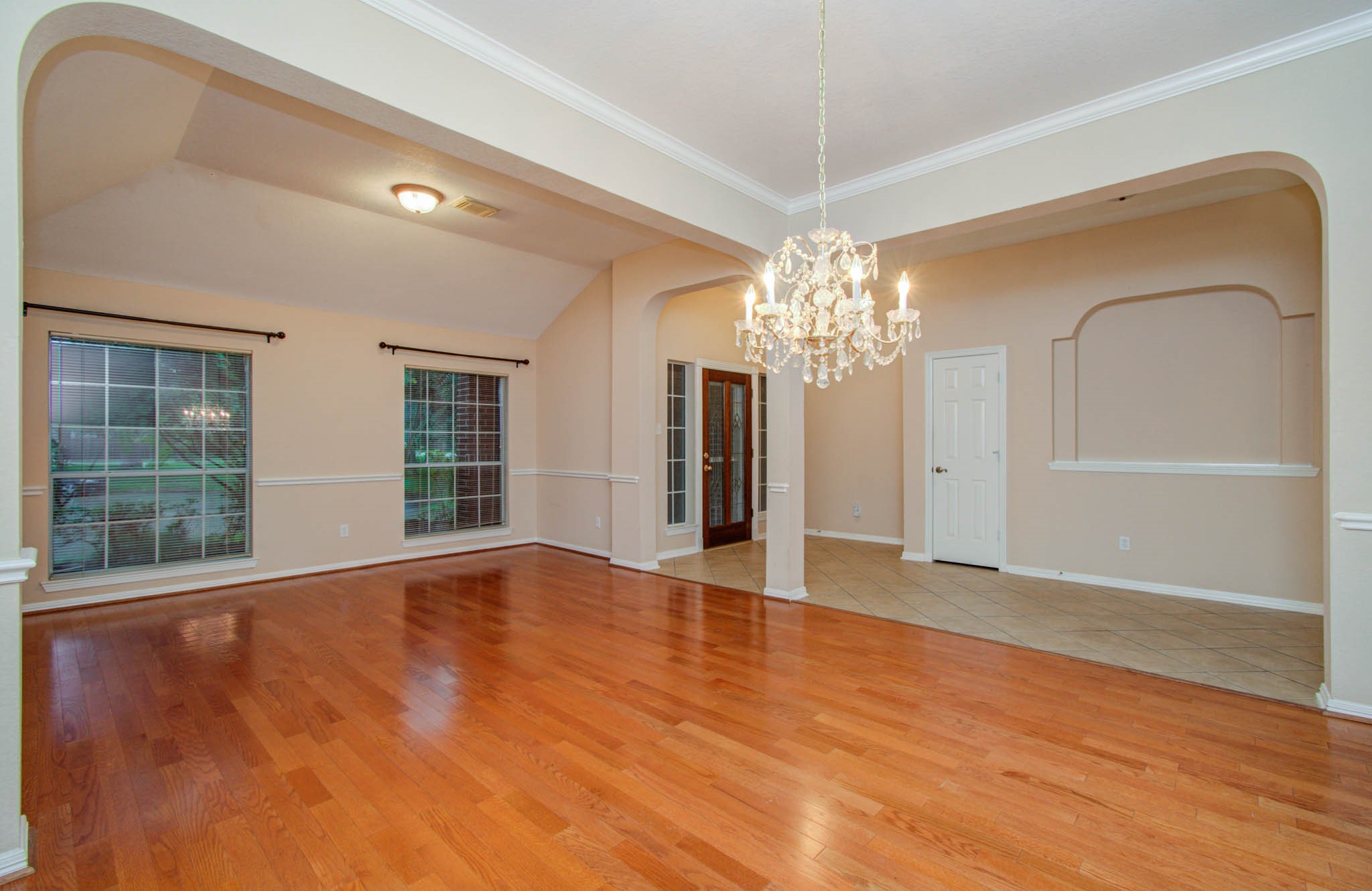 Elegant open living space featuring gleaming hardwood floors, a stunning chandelier, and large windows providing ample natural light.