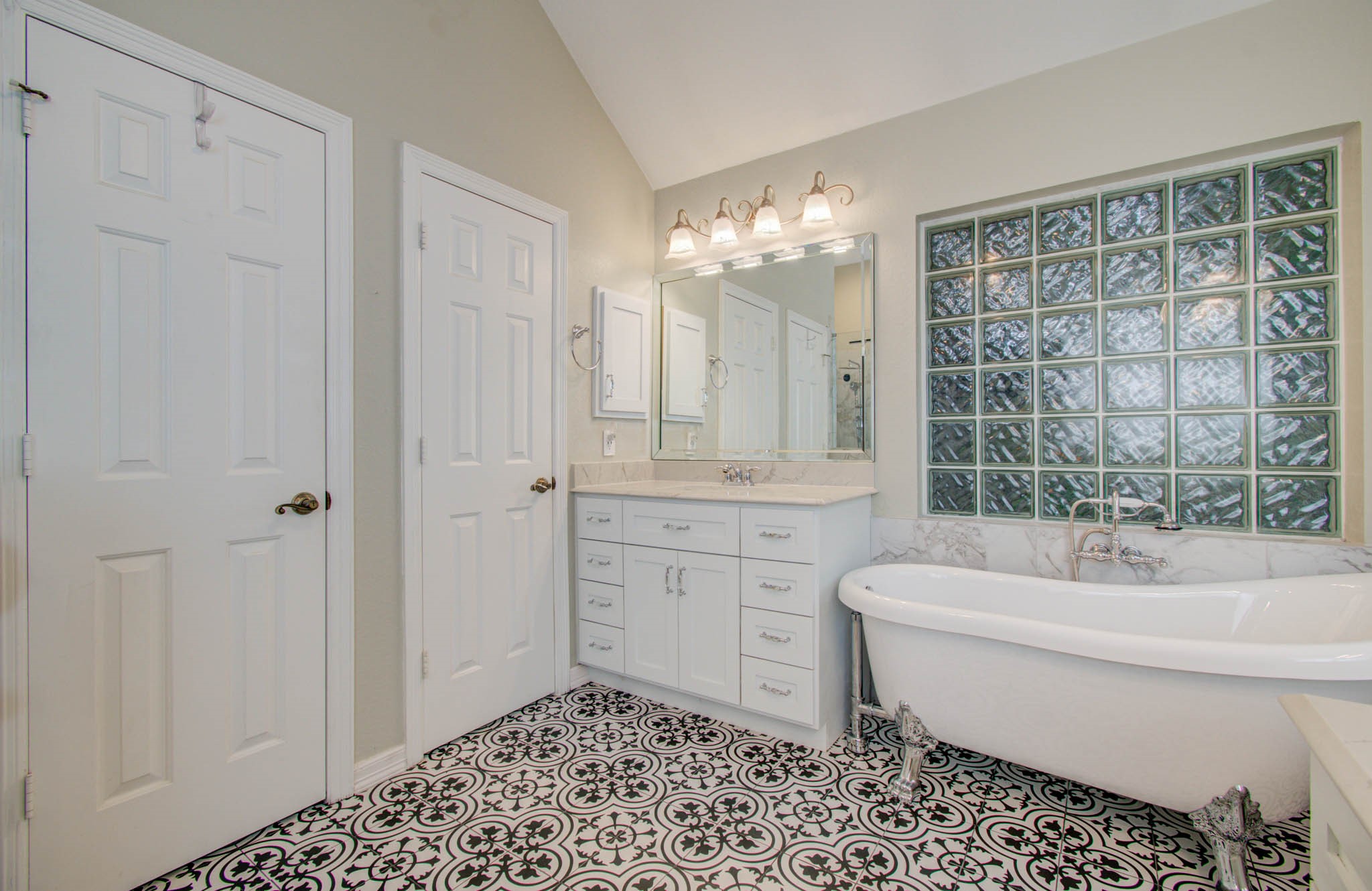 Elegant bathroom featuring a classic clawfoot tub, stylish patterned floor tiles, and ample natural light through glass block windows.