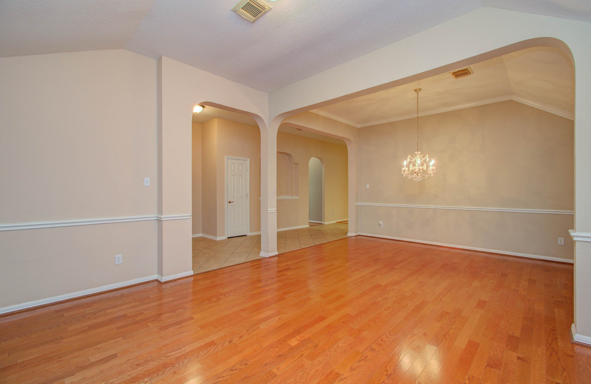 Elegant open-concept living space with warm wood flooring, arched entryways, and a sparkling chandelier, perfect for entertaining.