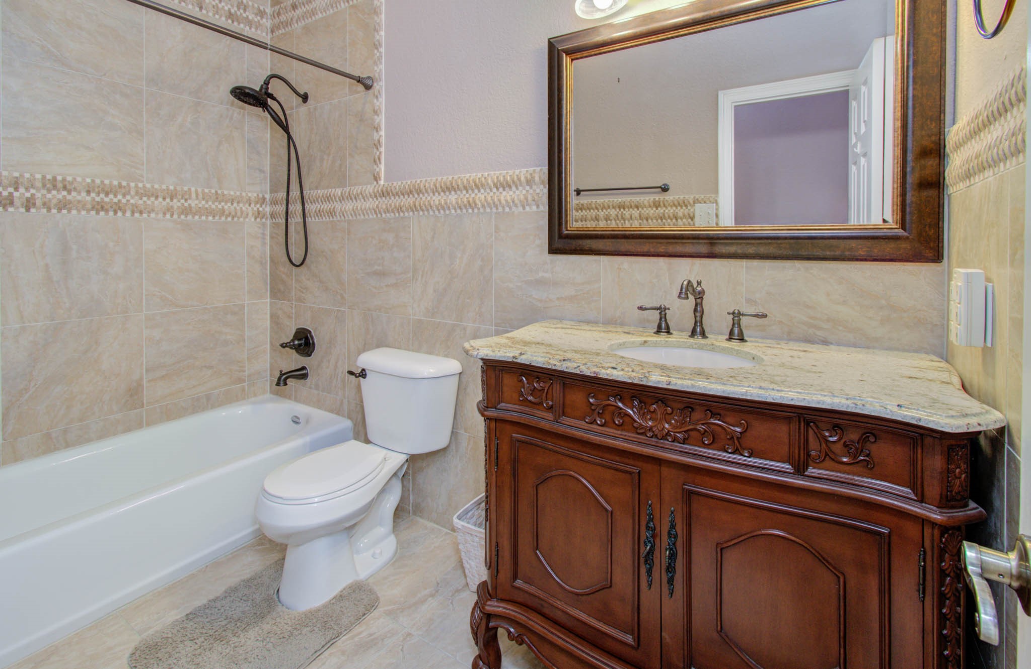 Elegant bathroom featuring a luxurious granite-topped vanity with ornate wood detailing, complemented by a stylish tiled shower and bath.