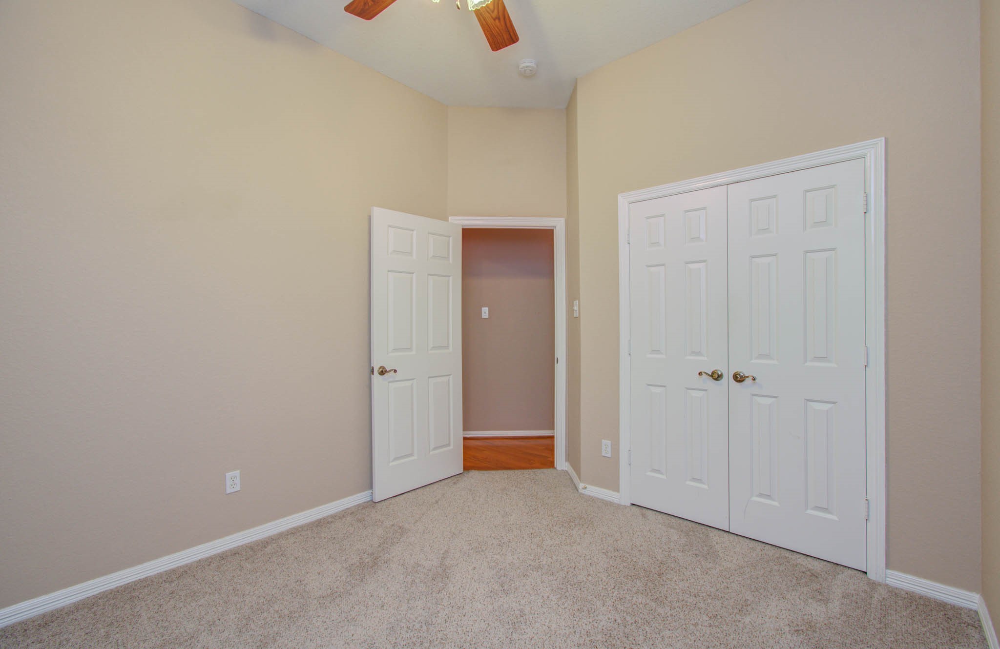 Cozy room with neutral walls, plush carpet, and ample closet space, illuminated by a ceiling fan light.