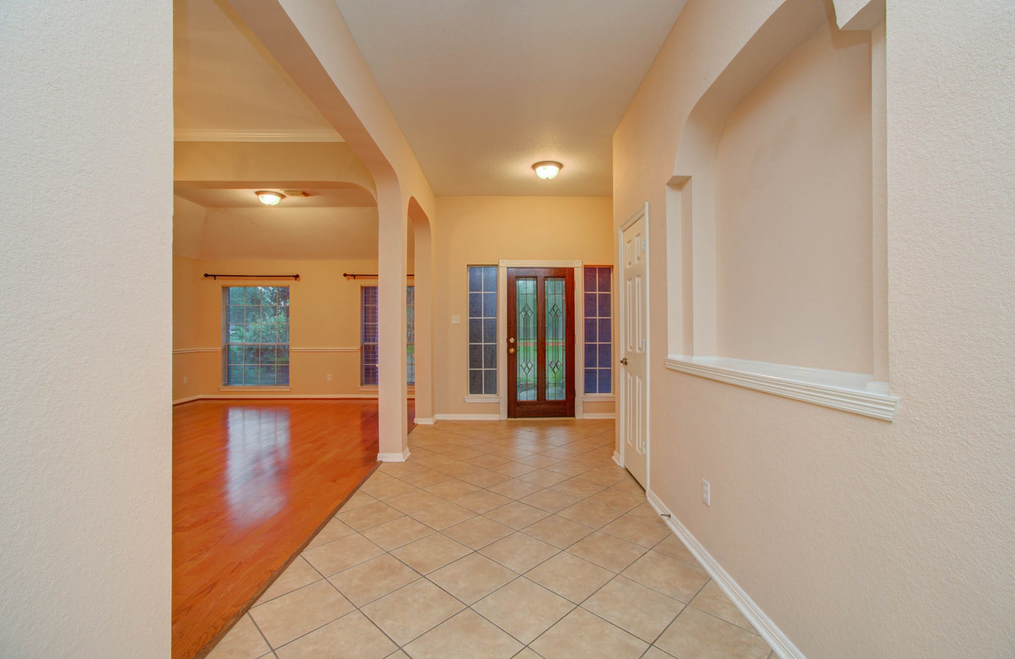 Inviting entryway with elegant tile flooring leads to a spacious living area featuring warm wood floors and large windows for natural light.