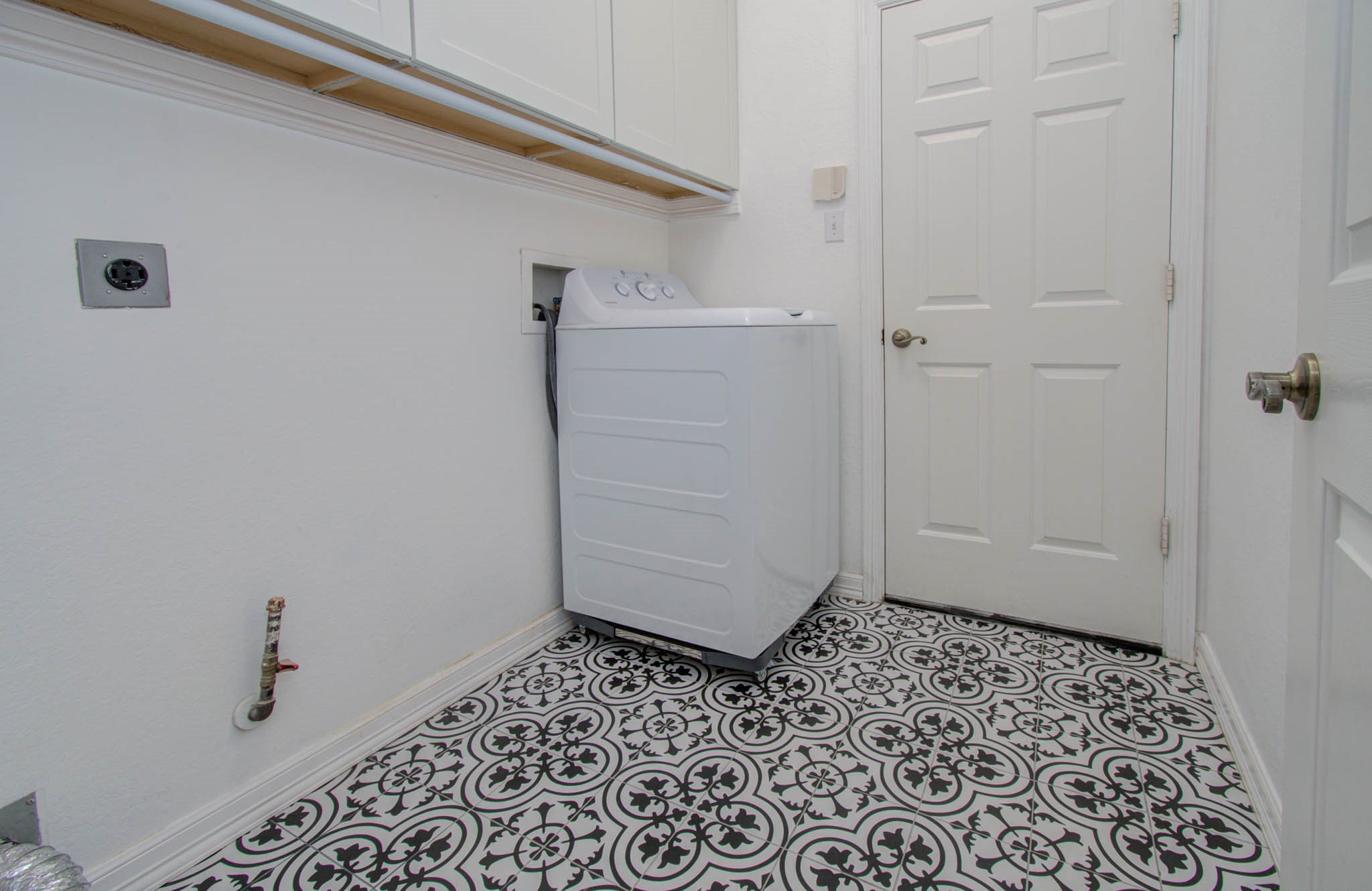 Charming laundry room featuring elegant patterned tile flooring, ample cabinet storage, and a convenient layout.