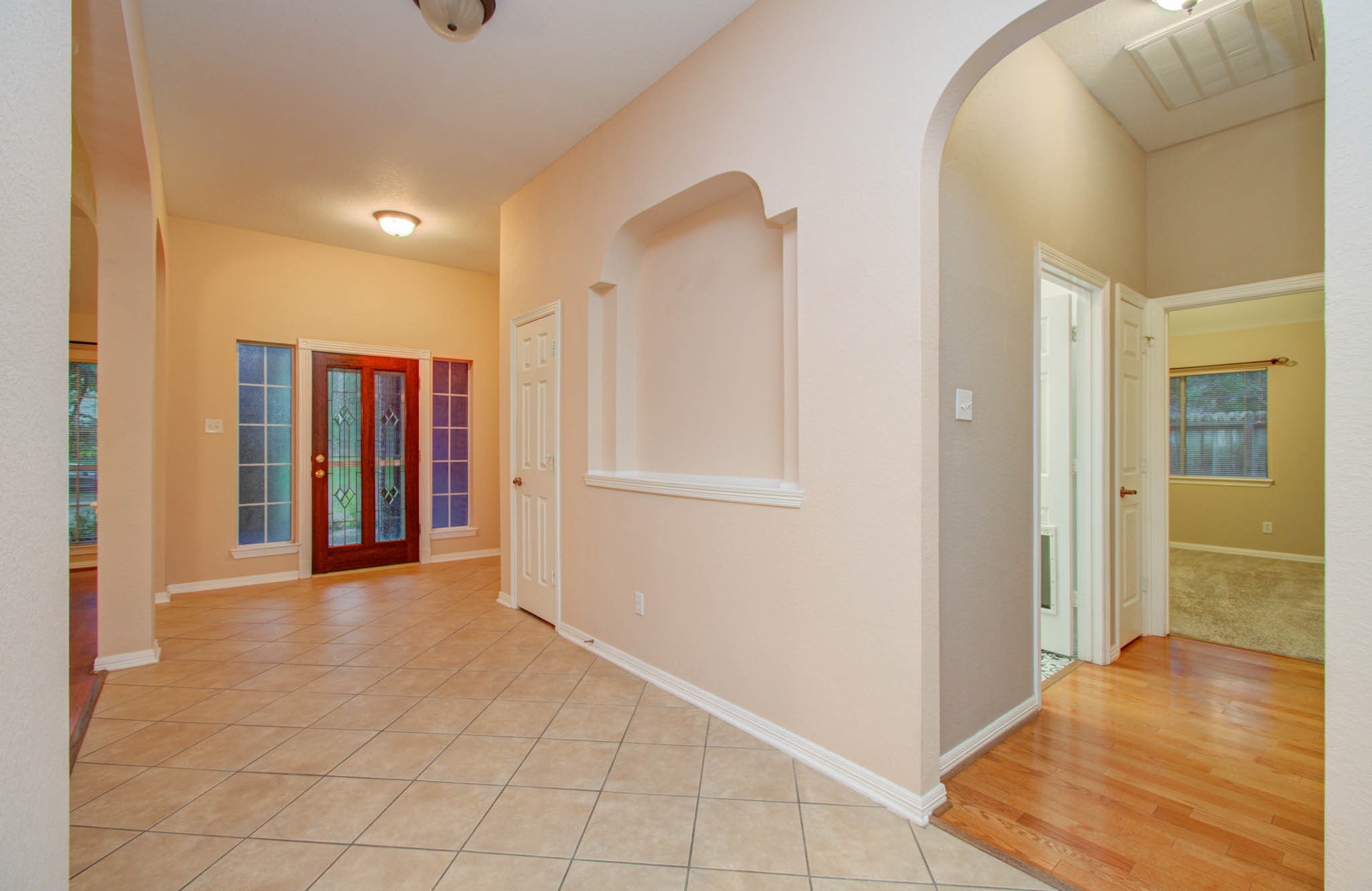 Inviting entryway with elegant tiled flooring, beautiful glass-paneled double doors, and an arched hallway leading to cozy rooms, combining functionality with charm.