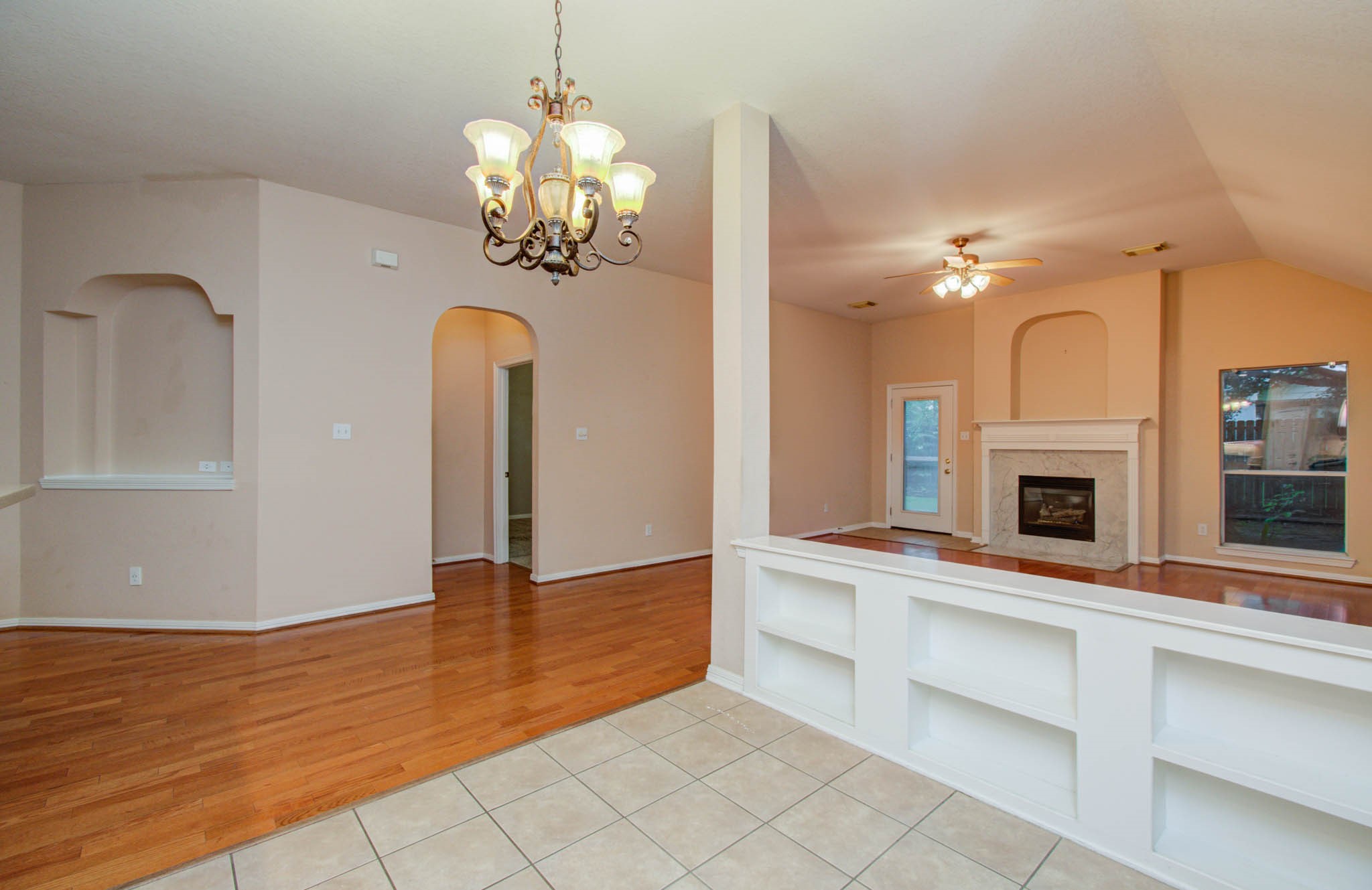 Spacious open living area features elegant wood flooring, a cozy fireplace, and built-in shelving, complemented by a stylish chandelier and abundant natural light.