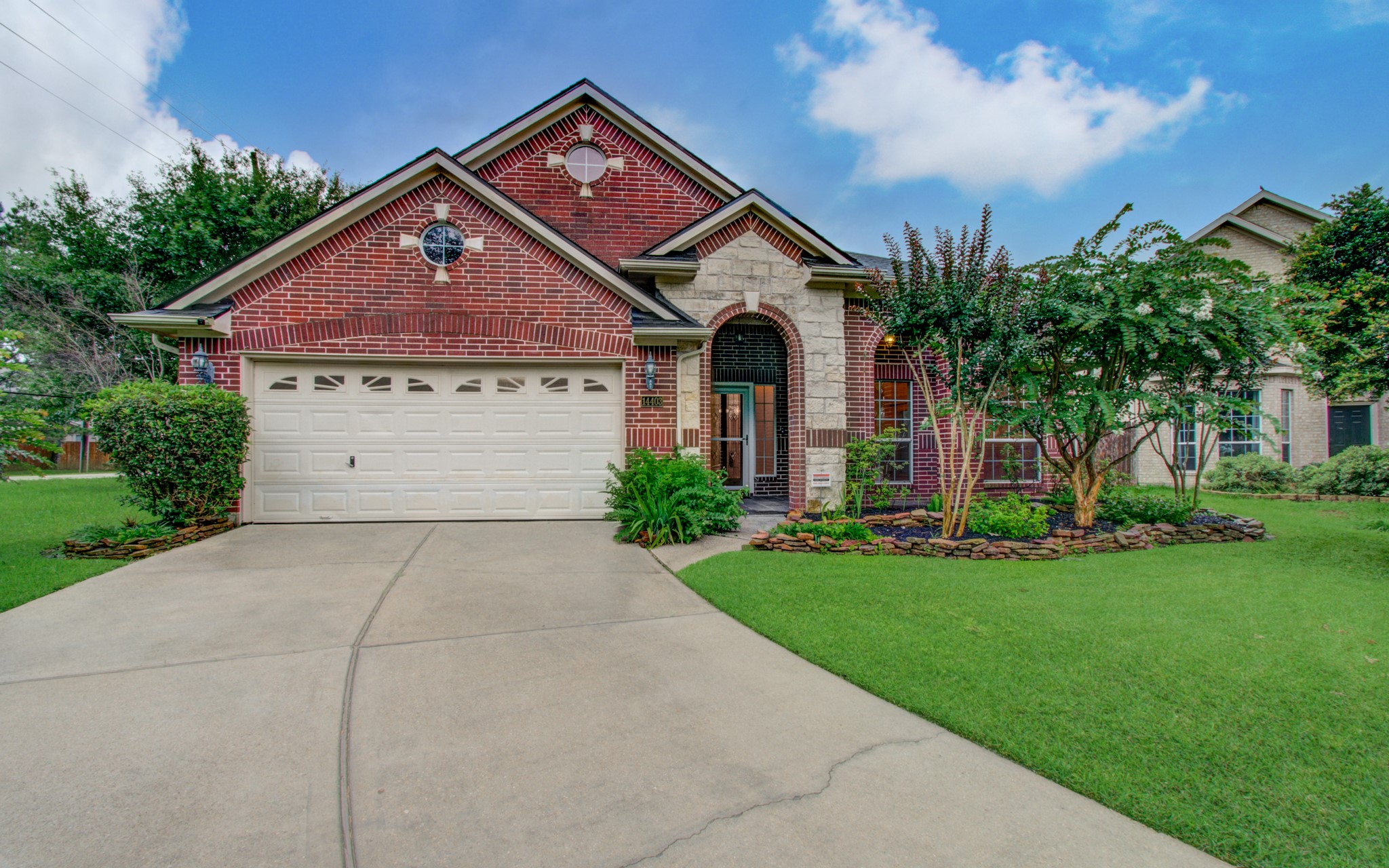 Charming red brick home with a welcoming arched entryway, lush landscaping, and a spacious two-car garage.