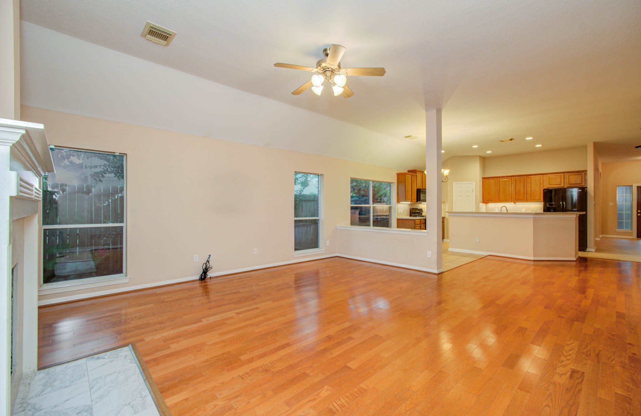 Spacious open-concept living area with warm hardwood floors, a cozy fireplace, and a modern kitchen featuring a large breakfast bar and sleek appliances. Abundant natural light enhances the welcoming atmosphere.