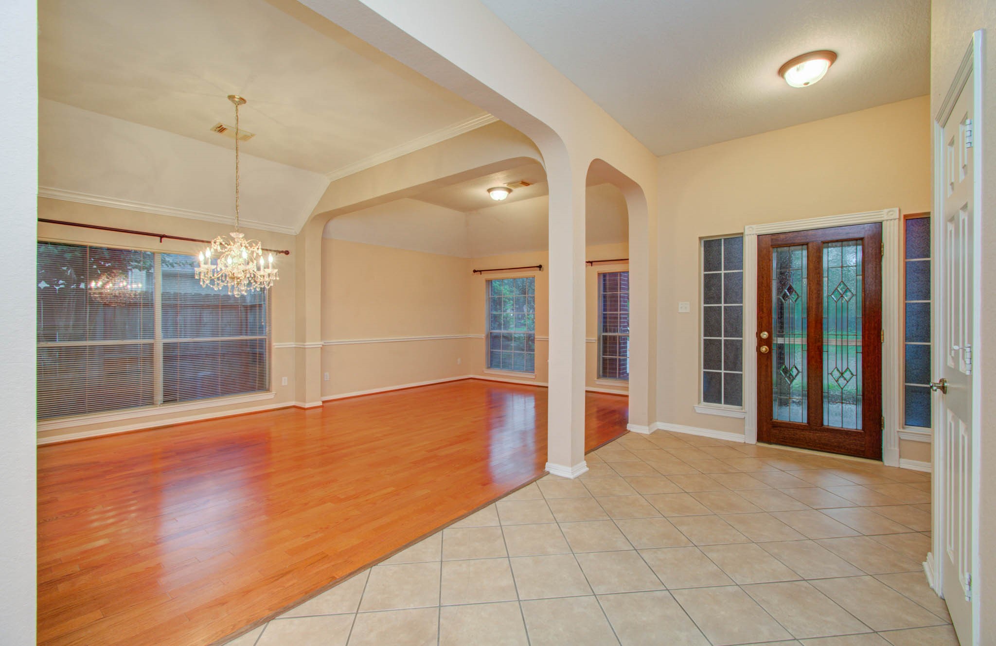 Elegant entryway with a tiled floor and decorative glass door leads to a spacious living area featuring warm wood flooring and a sparkling chandelier, perfect for entertaining.