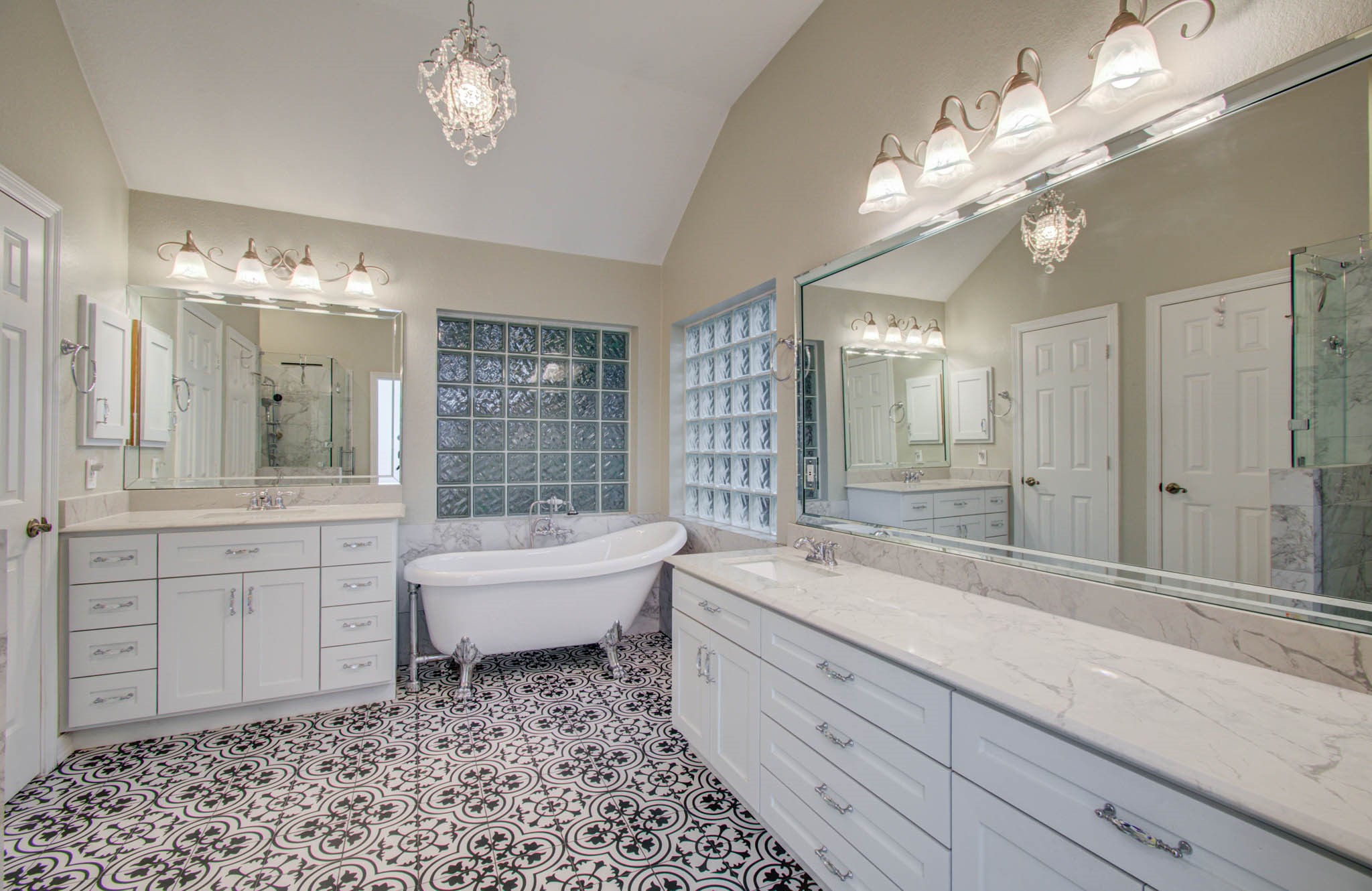 Elegant bathroom featuring a luxurious clawfoot tub, dual vanities with marble countertops, and chic patterned tile flooring.