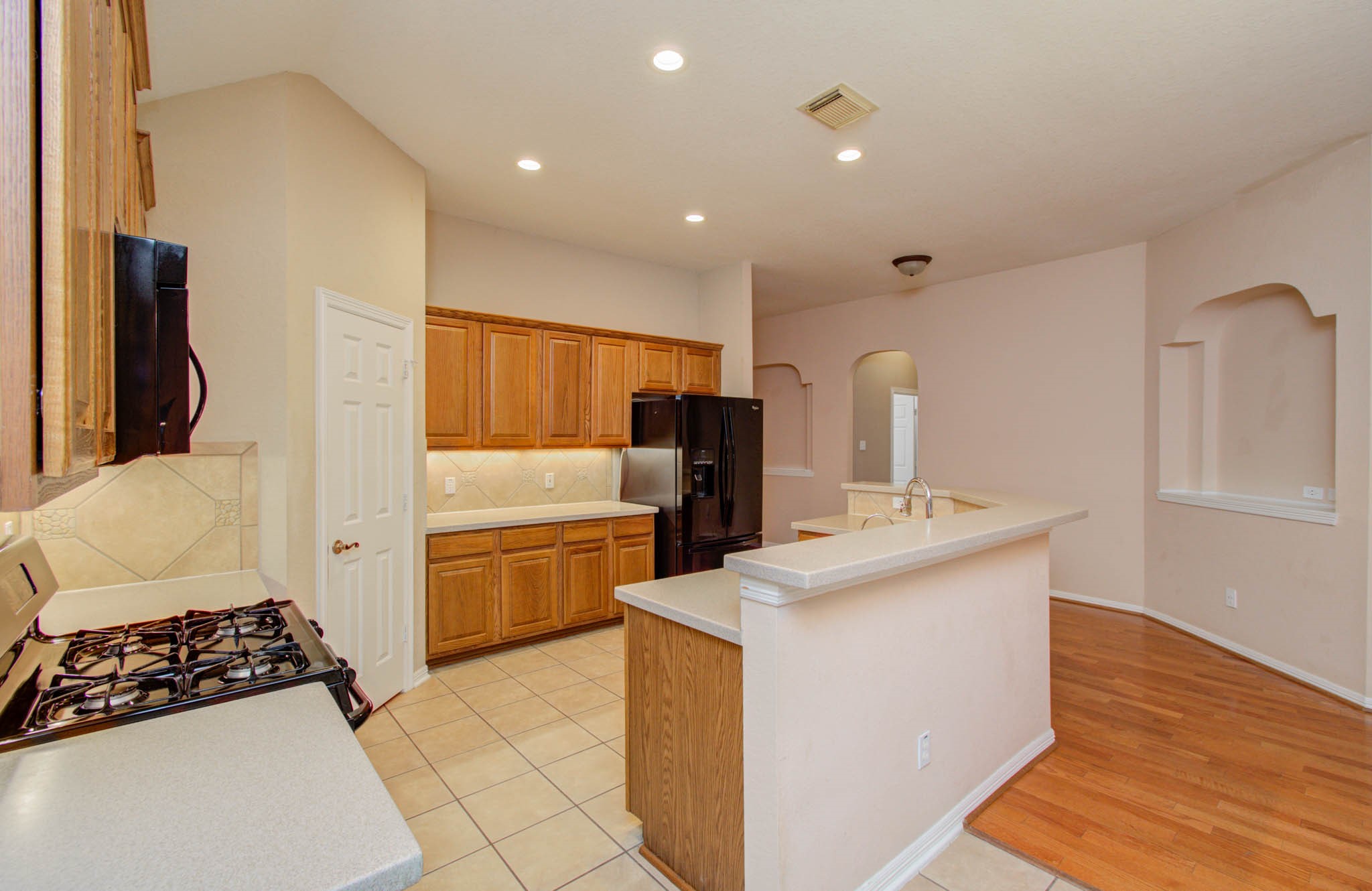 Bright and spacious kitchen with modern appliances, ample cabinetry, and a convenient breakfast bar, seamlessly flowing into an open living area with elegant hardwood flooring.