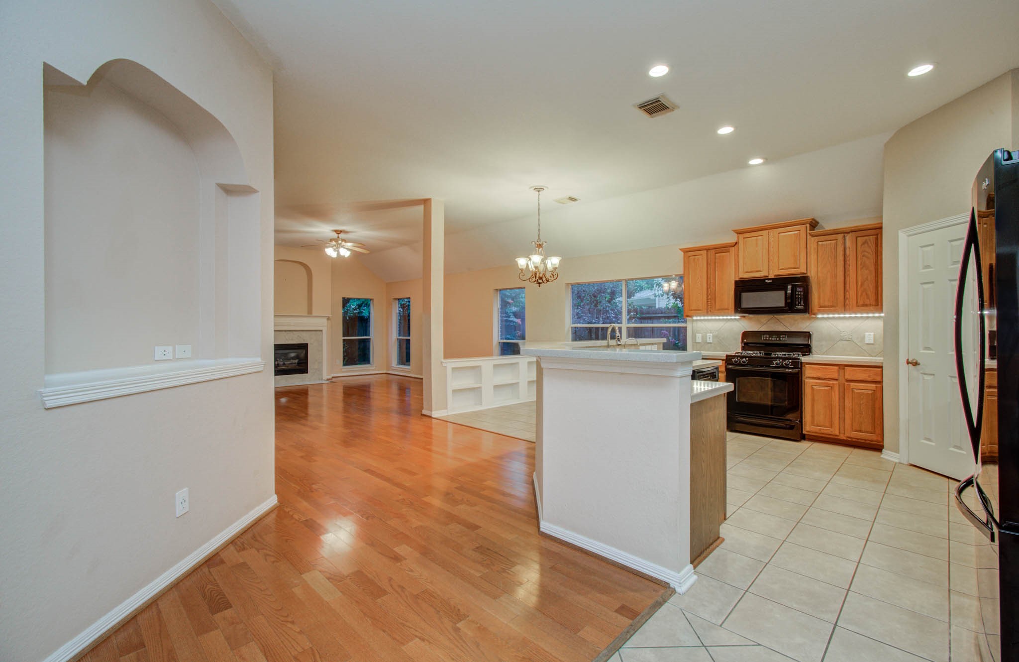 Spacious open-concept kitchen and living area featuring warm hardwood floors, a cozy fireplace, and abundant natural light. The kitchen boasts modern appliances, ample cabinetry, and a convenient breakfast bar.
