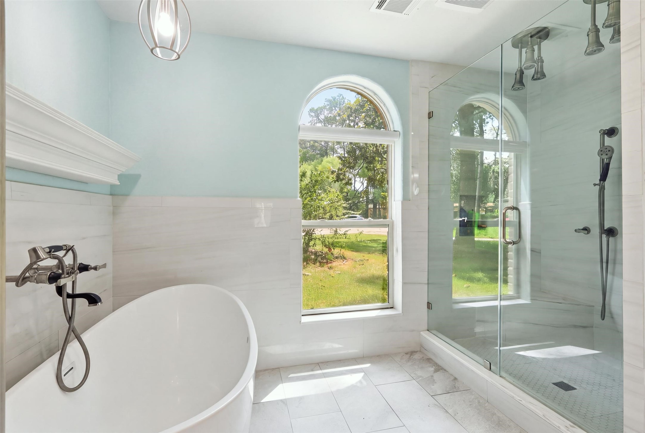 Spa-like primary bath featuring a freestanding soaking tub and oversized glass-enclosed shower with multiple shower heads.