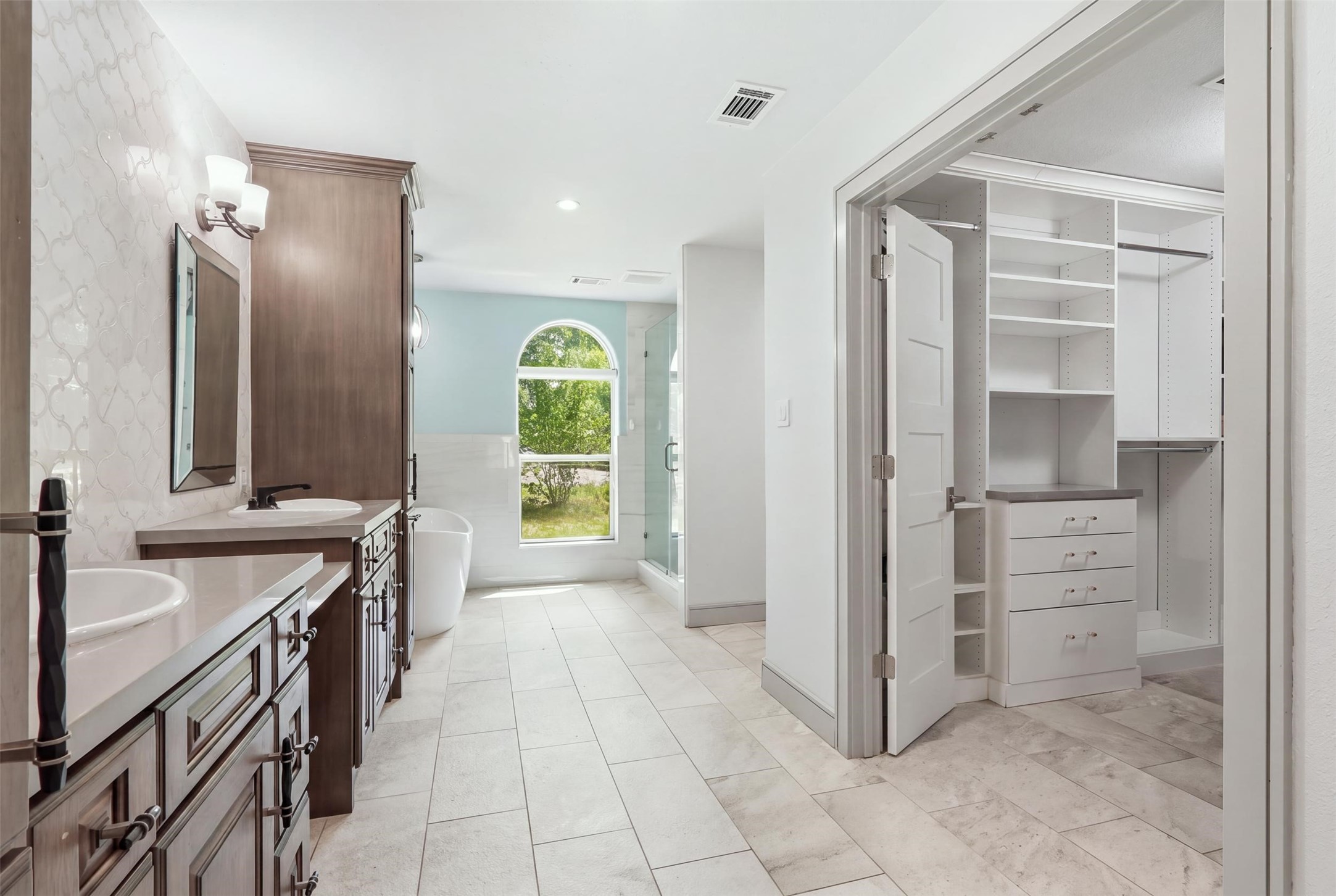 Spa-like primary bath featuring dual vanities, a freestanding soaking tub, walk-in shower, and spacious custom closet.