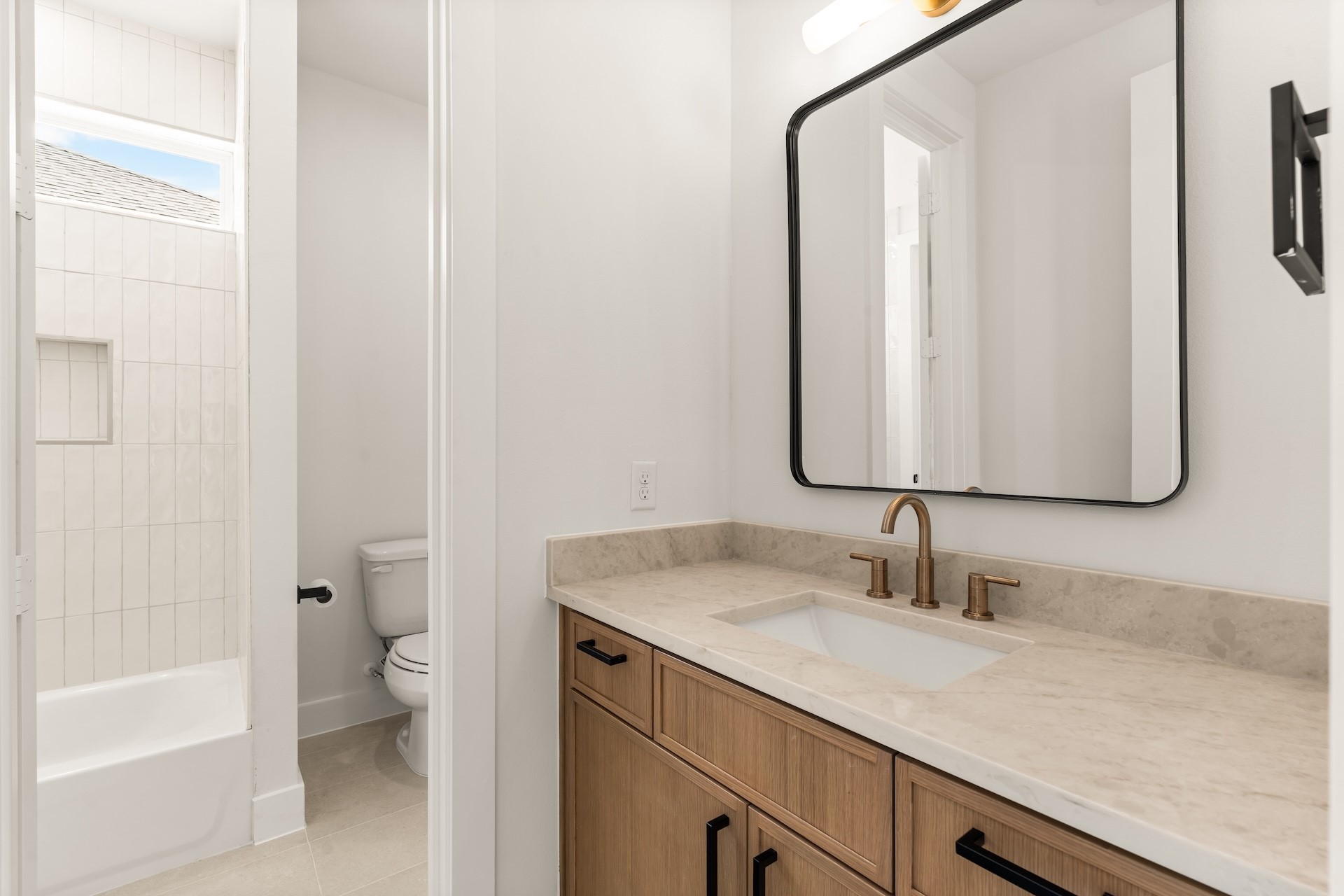Full secondary bathroom with a modern vanity, warm brass accents, and custom tile surround.