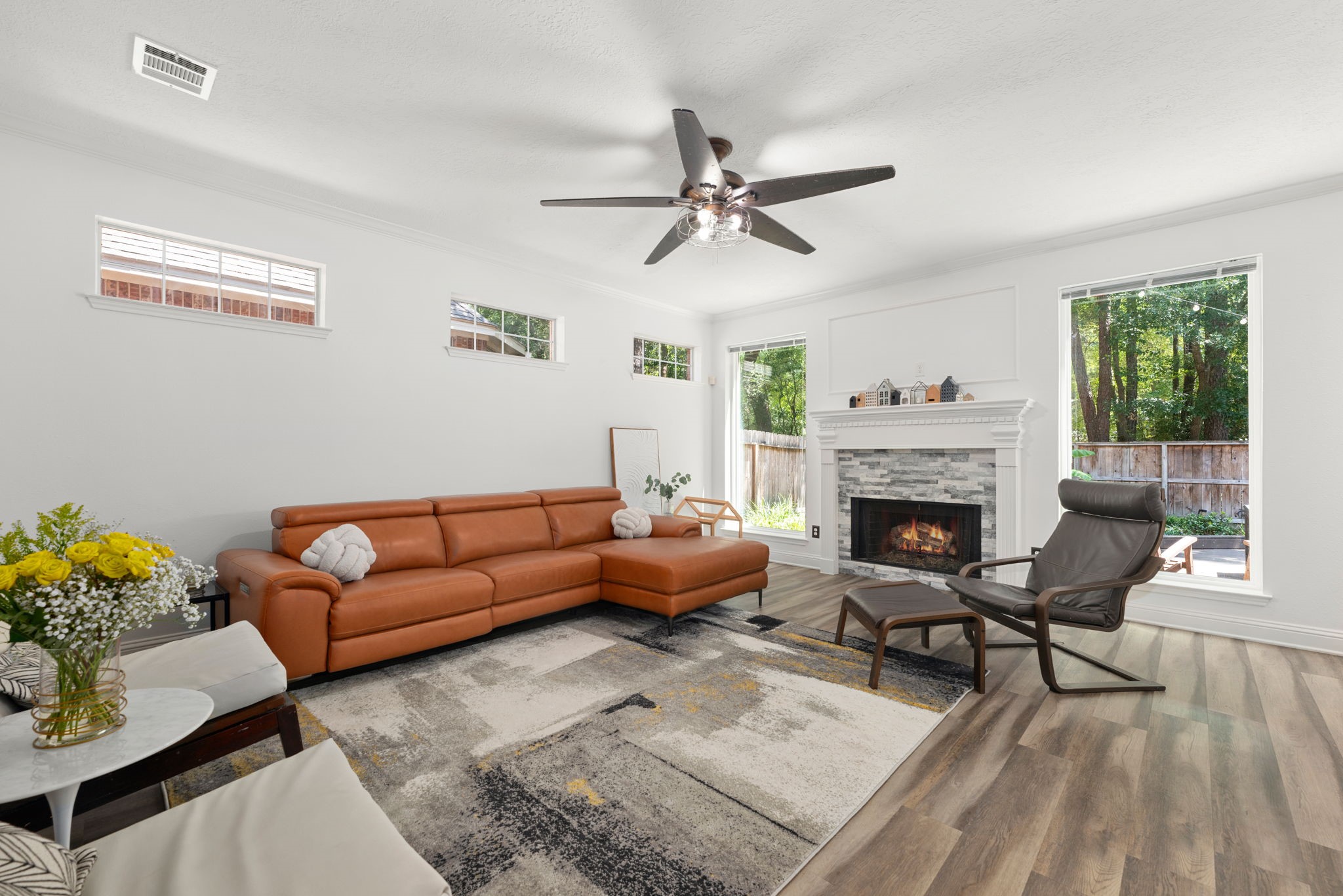 Spacious living room featuring a cozy fireplace, elegant wood fllooring, and abundant natural light from large windows.