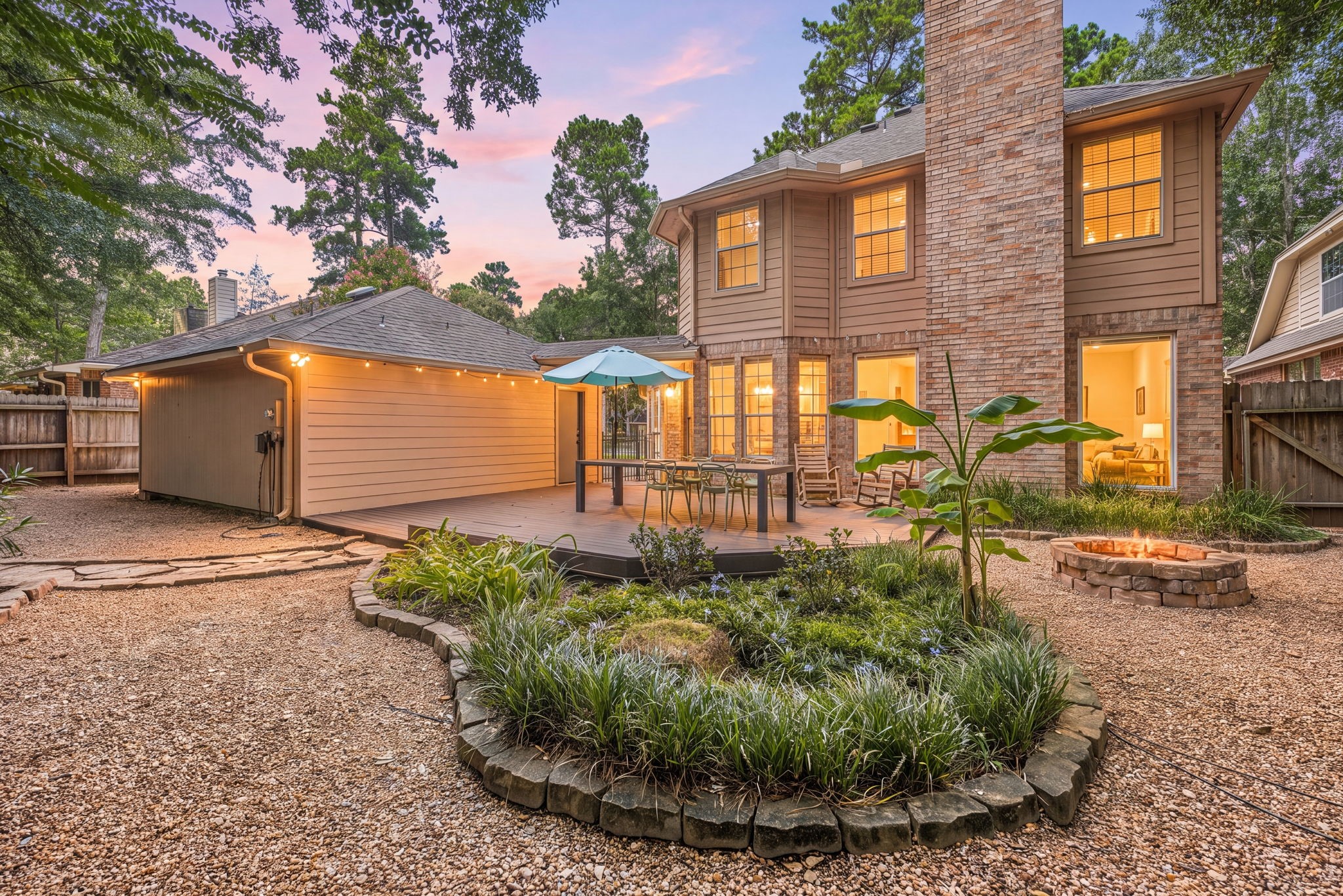 Charming back yard oasis featuring a spacious deck with seating. Surrounded by lush greenery and cozy fire pit.