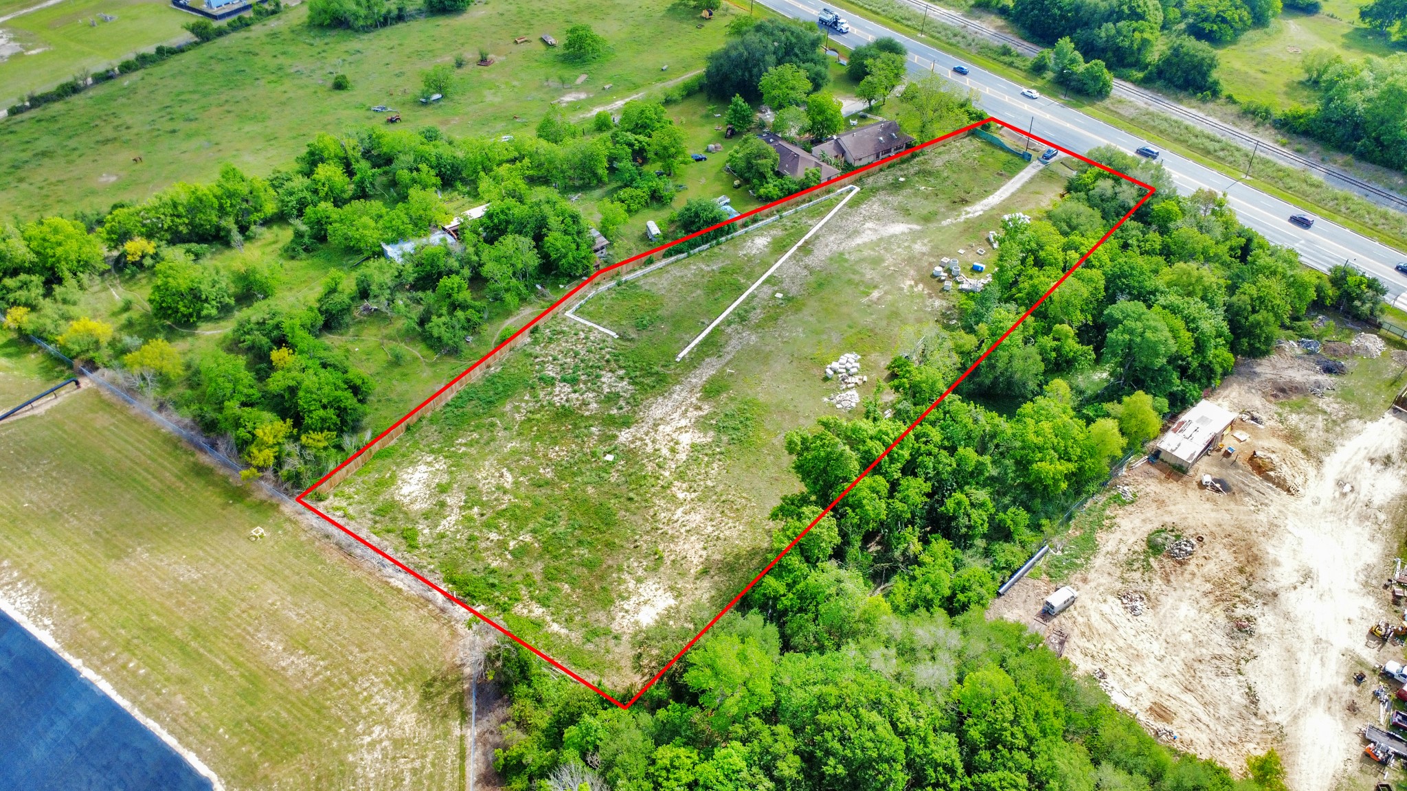 Expansive plot of land bordered by lush greenery, with a clear demarcation line. It features a house near a main road, offering easy access. Ideal for development or a private estate.