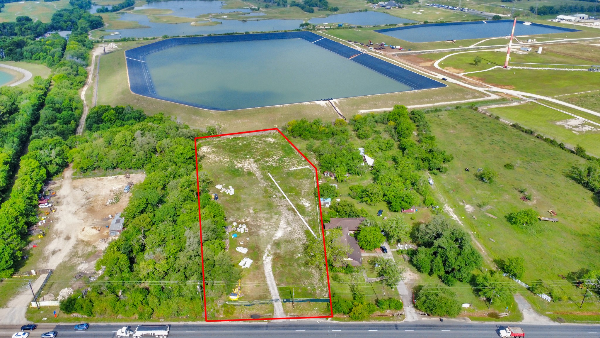 This aerial photo showcases a spacious plot of land outlined in red, situated near a large reservoir. The area is surrounded by greenery, with a mix of open space and some trees. Access is via a nearby road, offering potential for development or a private retreat.