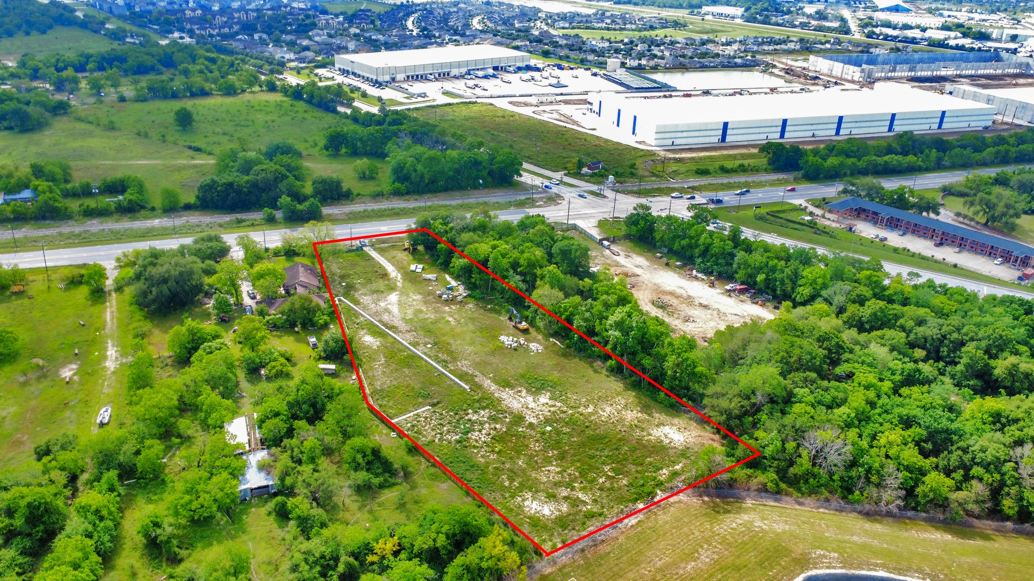 Spacious plot of land outlined in red, located near a main road. Surrounded by lush greenery and adjacent to commercial and residential areas. Ideal for development with convenient access to nearby amenities.