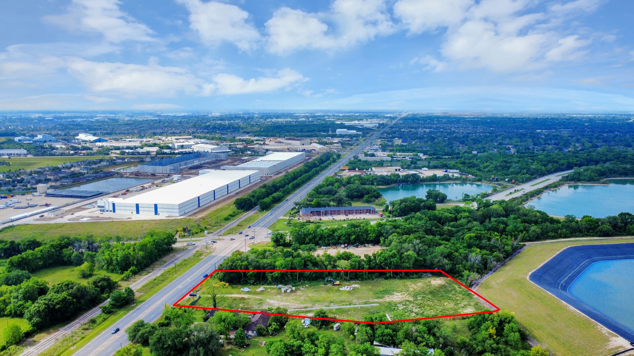 This aerial photo showcases a spacious plot of land outlined in red, with lush greenery surrounding it. It is located near a major road, with industrial buildings and water bodies nearby, offering both accessibility and scenic views.