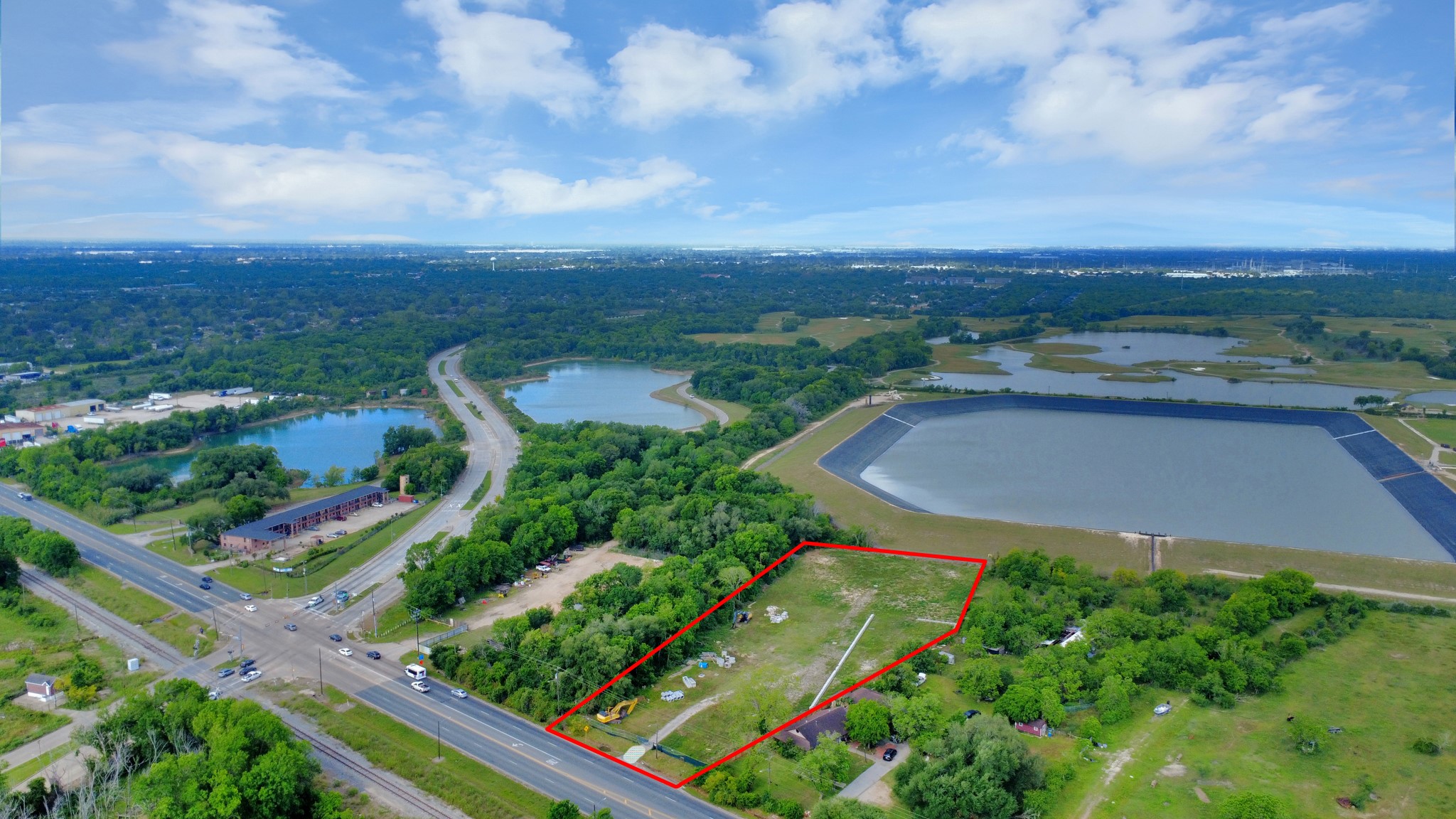 This photo showcases a spacious plot of land outlined in red, located near a main road and surrounded by lush greenery. It offers proximity to a large water reservoir and has easy access to nearby amenities. Ideal for buyers seeking a serene yet accessible location.