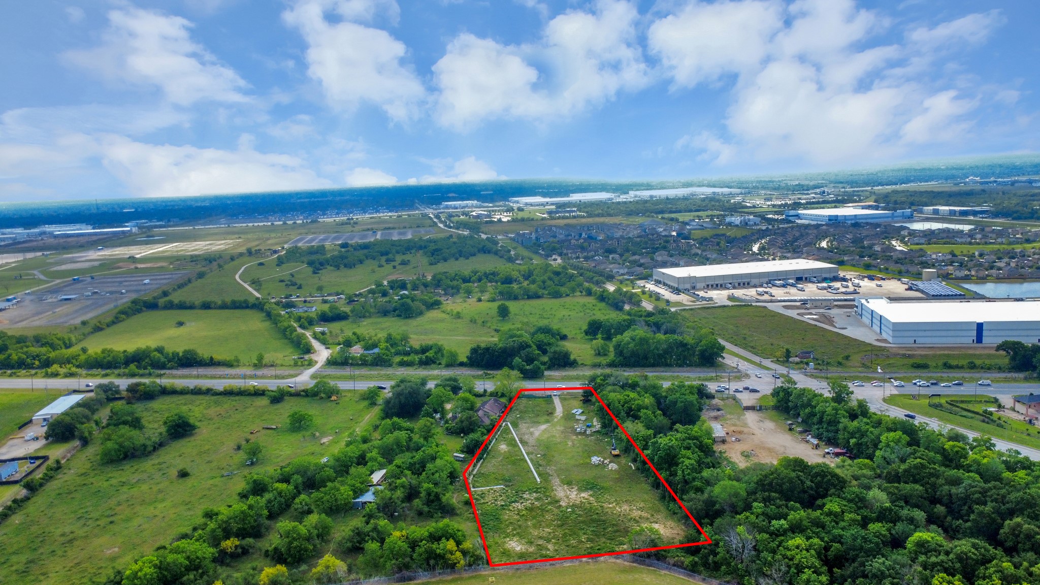 This aerial photo shows a spacious plot of land outlined in red, surrounded by greenery. It's situated near a road and close to commercial buildings, offering a blend of natural beauty and accessibility. Ideal for development or building a home with convenient access to amenities.