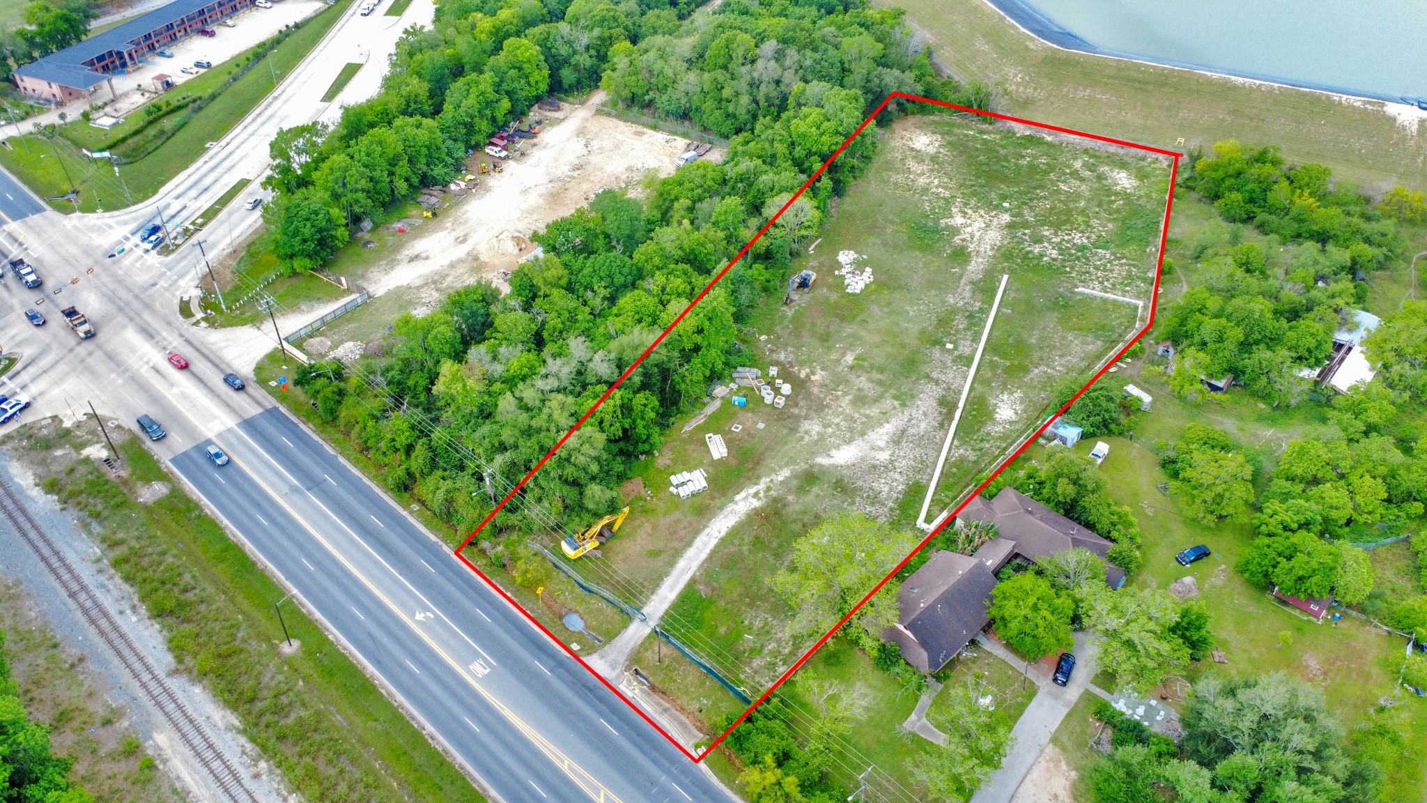 This aerial photo showcases a large, rectangular plot of land bordered in red, featuring a mix of open space and trees. It includes a house, access to a main road, and proximity to a body of water, making it ideal for development or a private residence. This aerial photo showcases a large, rectangular plot of land bordered in red, featuring a mix of open space and trees. It includes a house, access to a main road, and proximity to a body of water, making it ideal for development or a private residence.