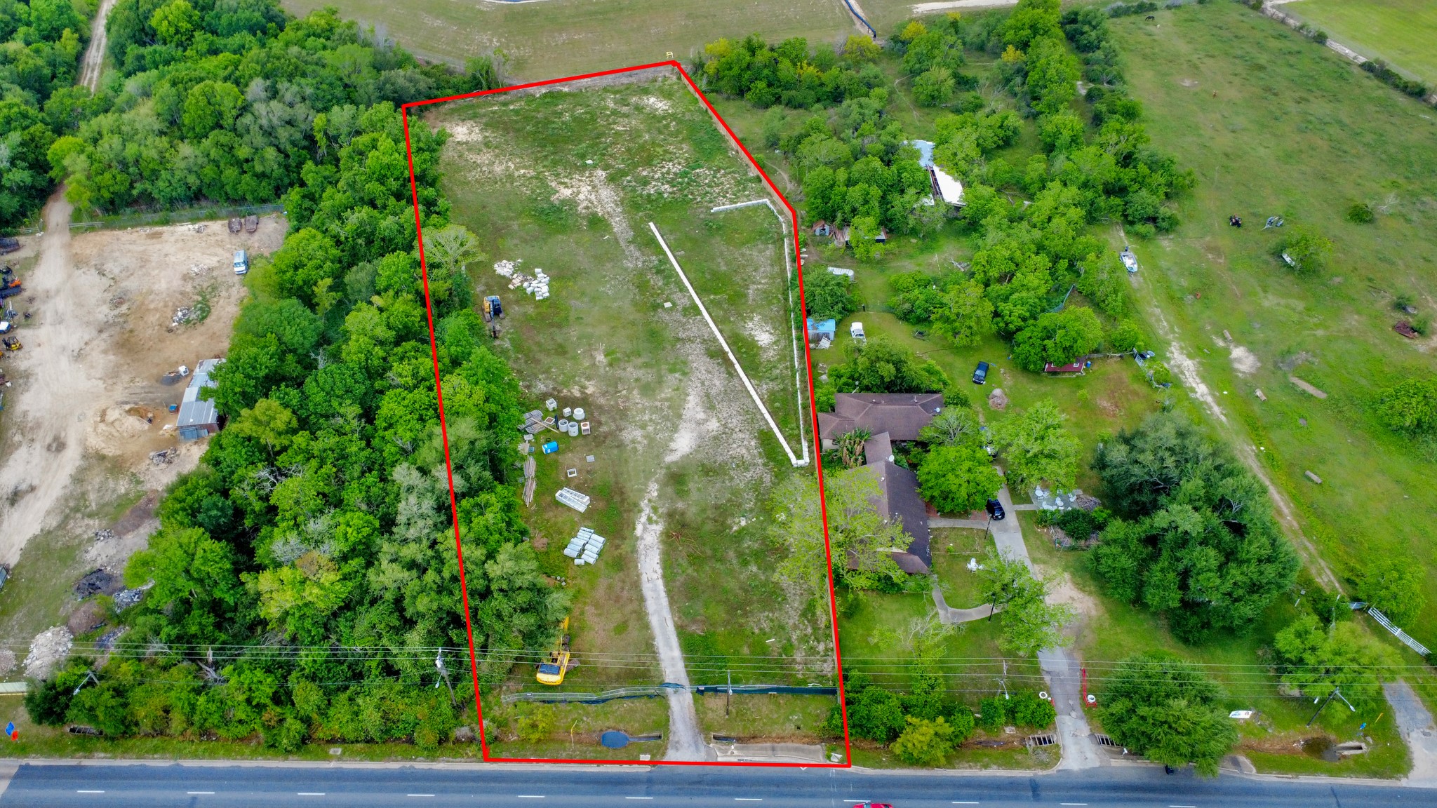 This aerial photo showcases a large, rectangular plot of land outlined in red, surrounded by lush greenery. The plot includes a mix of open space and trees, with a few structures visible. It borders a main road, offering easy access. Ideal for development or a private retreat. This aerial photo showcases a large, rectangular plot of land outlined in red, surrounded by lush greenery. The plot includes a mix of open space and trees, with a few structures visible. It borders a main road, offering easy access. Ideal for development or a private retreat.