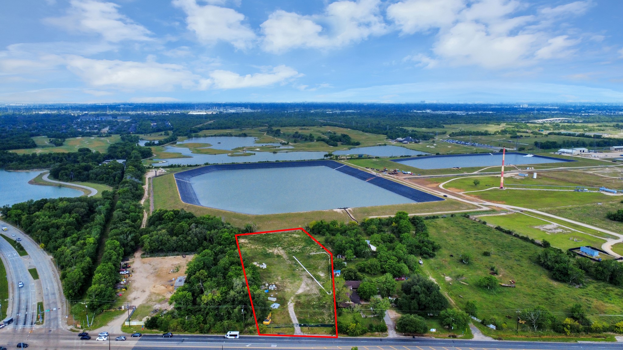 This aerial photo highlights a vast expanse of land outlined in red, surrounded by lush greenery and adjacent to large water bodies. The area has nearby roads and open spaces, offering a serene yet accessible location for potential development or home building.