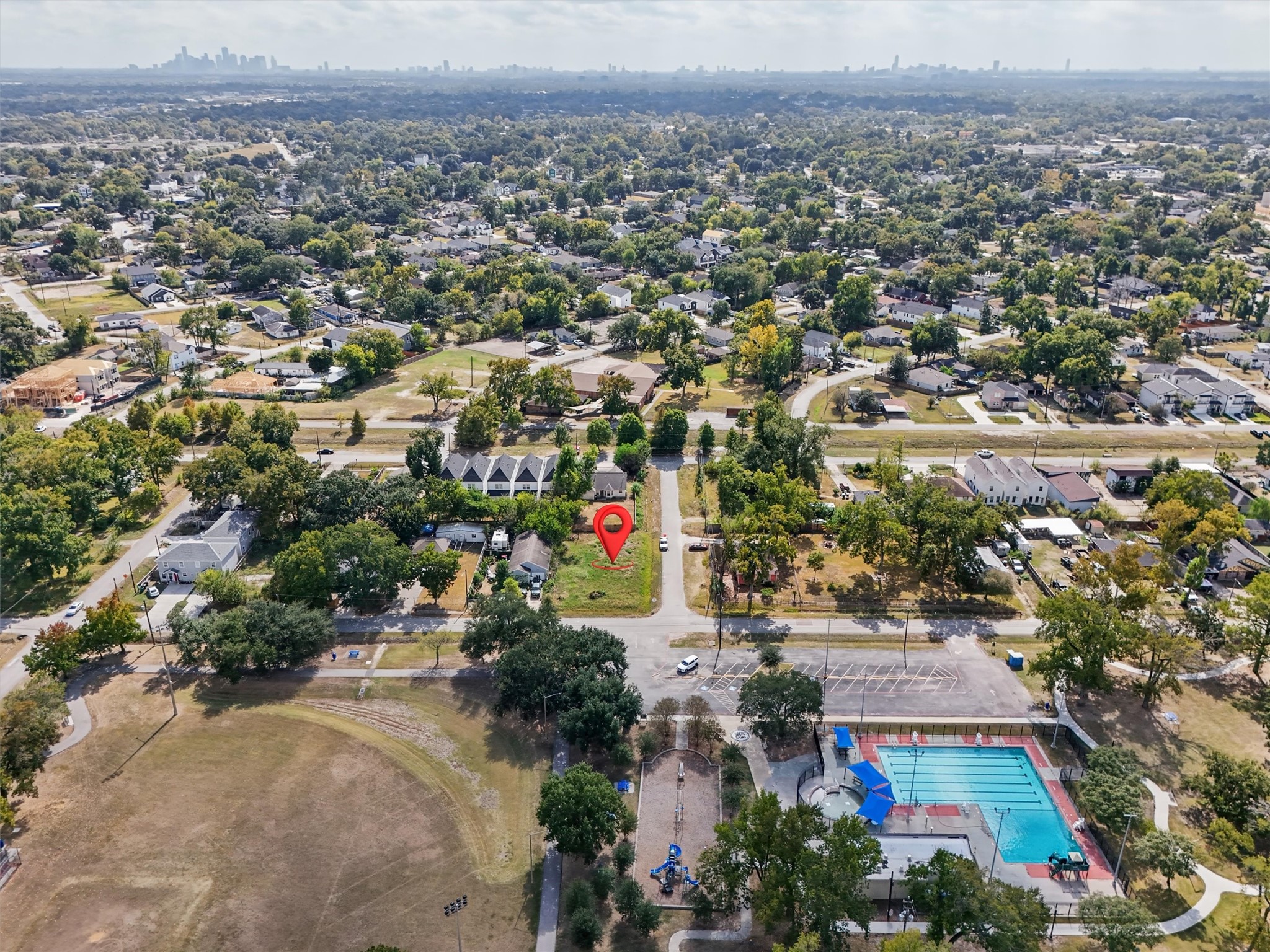 Location, location, location! This aerial view highlights the cleared corner lot, identified by the red marker, and its surrounding established residential neighborhood. Enjoy close proximity to a community swimming pool, playground, recreational fields, walking paths, and open green spaces. The neighborhood features mature trees, a mix of traditional and newer homes, and convenient access to surrounding streets.