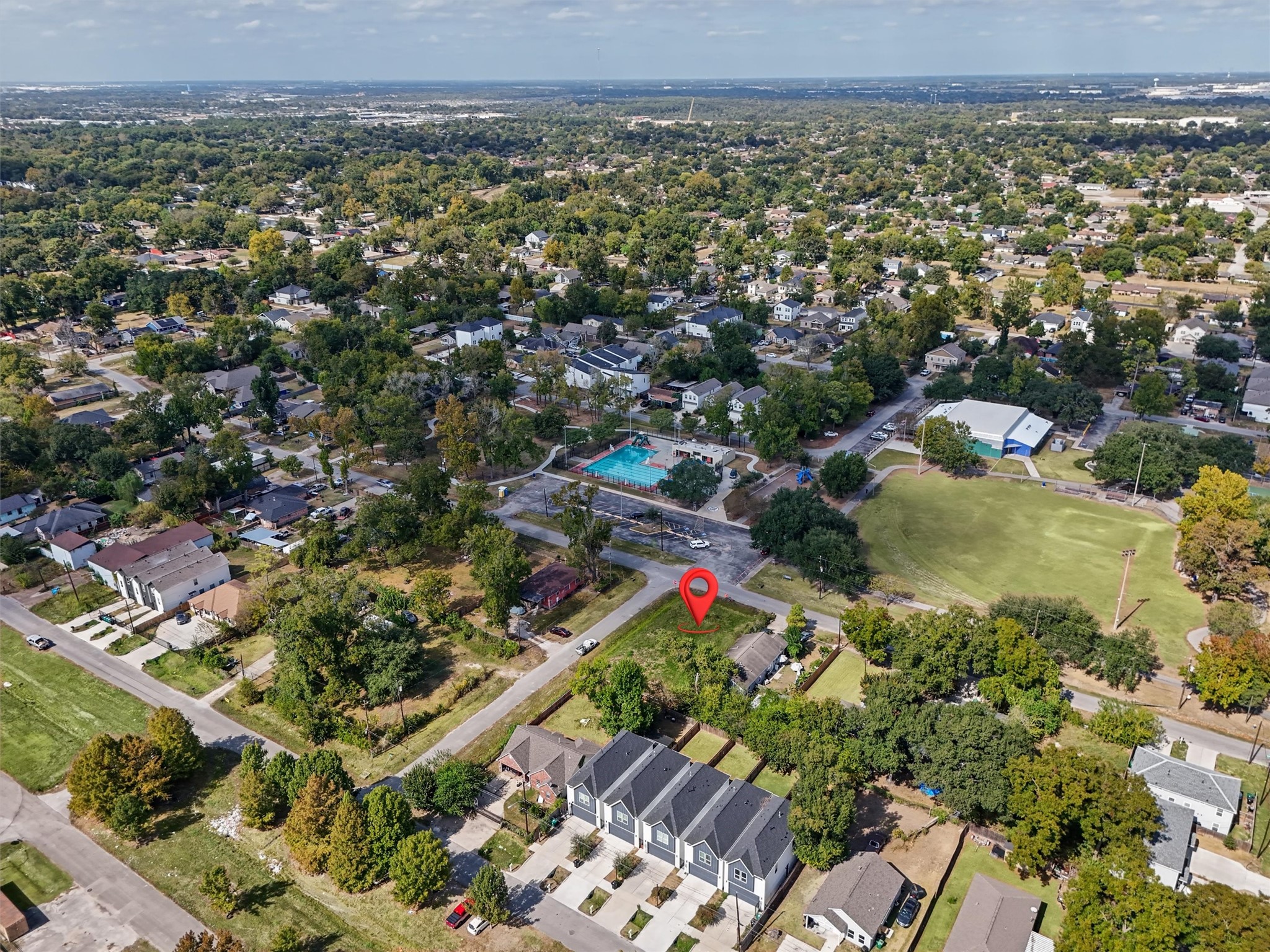 This cleared corner lot, highlighted by the red marker, is ideally situated in an established neighborhood surrounded by mature trees, beautiful homes, and newer construction. Located directly across from a community swimming pool, playground, recreational fields, and green spaces, this property offers a fantastic setting to build your dream home.