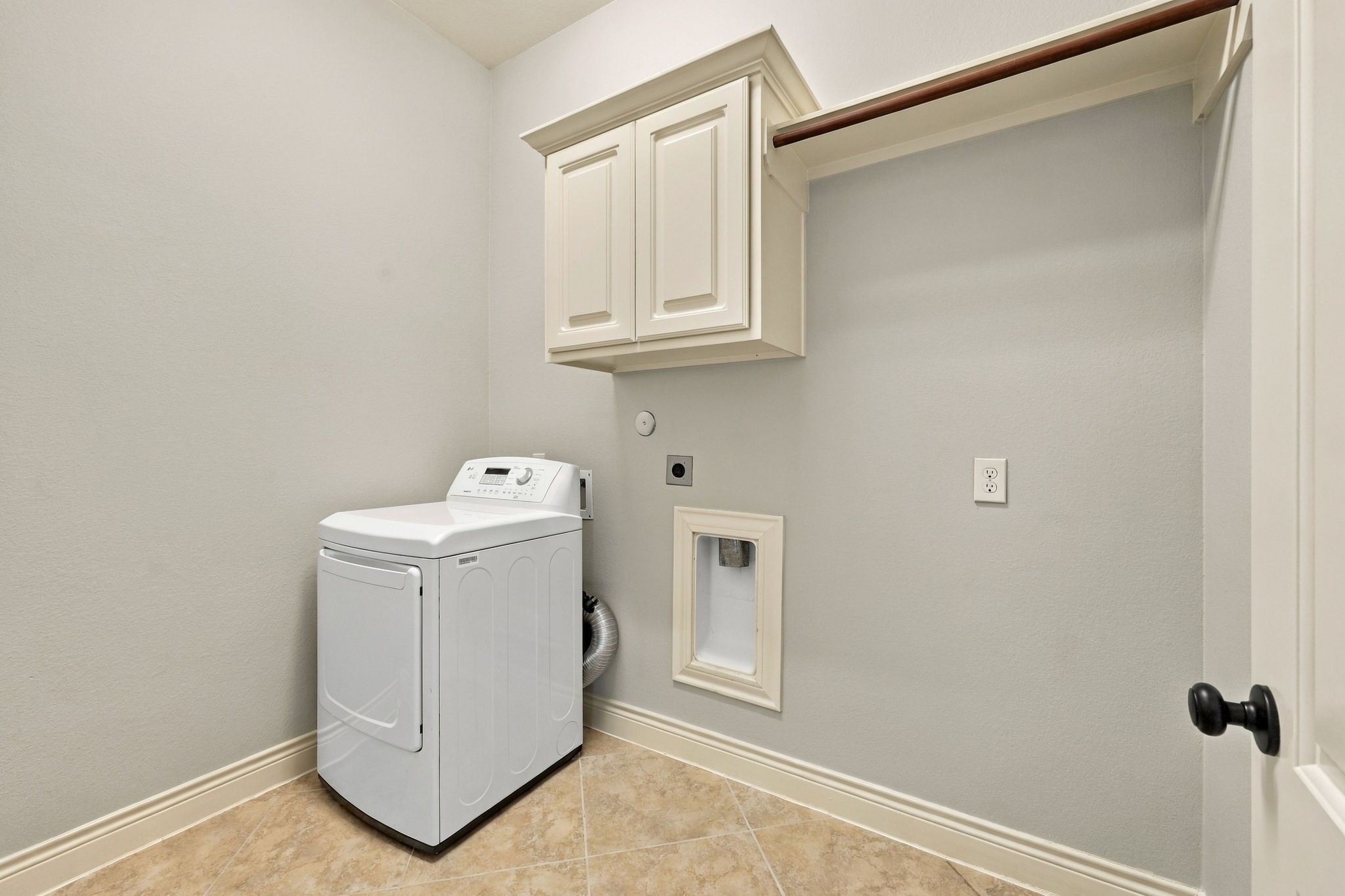 The spacious Laundry Room offers excellent functionality with built-in cabinetry, a hanging bar for air-drying clothes, and an additional storage shelf. There is also plenty of room to accommodate an extra refrigerator, providing added convenience and storage options for a busy household.