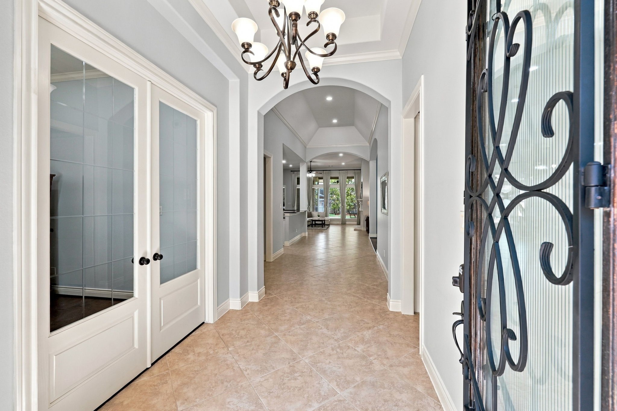 As you make your way inside, you are greeted by 18x18 tile flooring laid on a 45-degree angle and an impressive 13-foot ceiling in the foyer, highlighted by a striking eight-globe wrought-iron chandelier. Architectural arches add character and elegance, while double glass doors to the left open to the home office. The welcoming entryway offers an extended sightline through the home, creating an immediate sense of space and openness. As you make your way inside, you are greeted by 18x18 tile flooring laid on a 45-degree angle and an impressive 13-foot ceiling in the foyer, highlighted by a striking eight-globe wrought-iron chandelier. Architectural arches add character and elegance, while double glass doors to the left open to the home office. The welcoming entryway offers an extended sightline through the home, creating an immediate sense of space and openness.